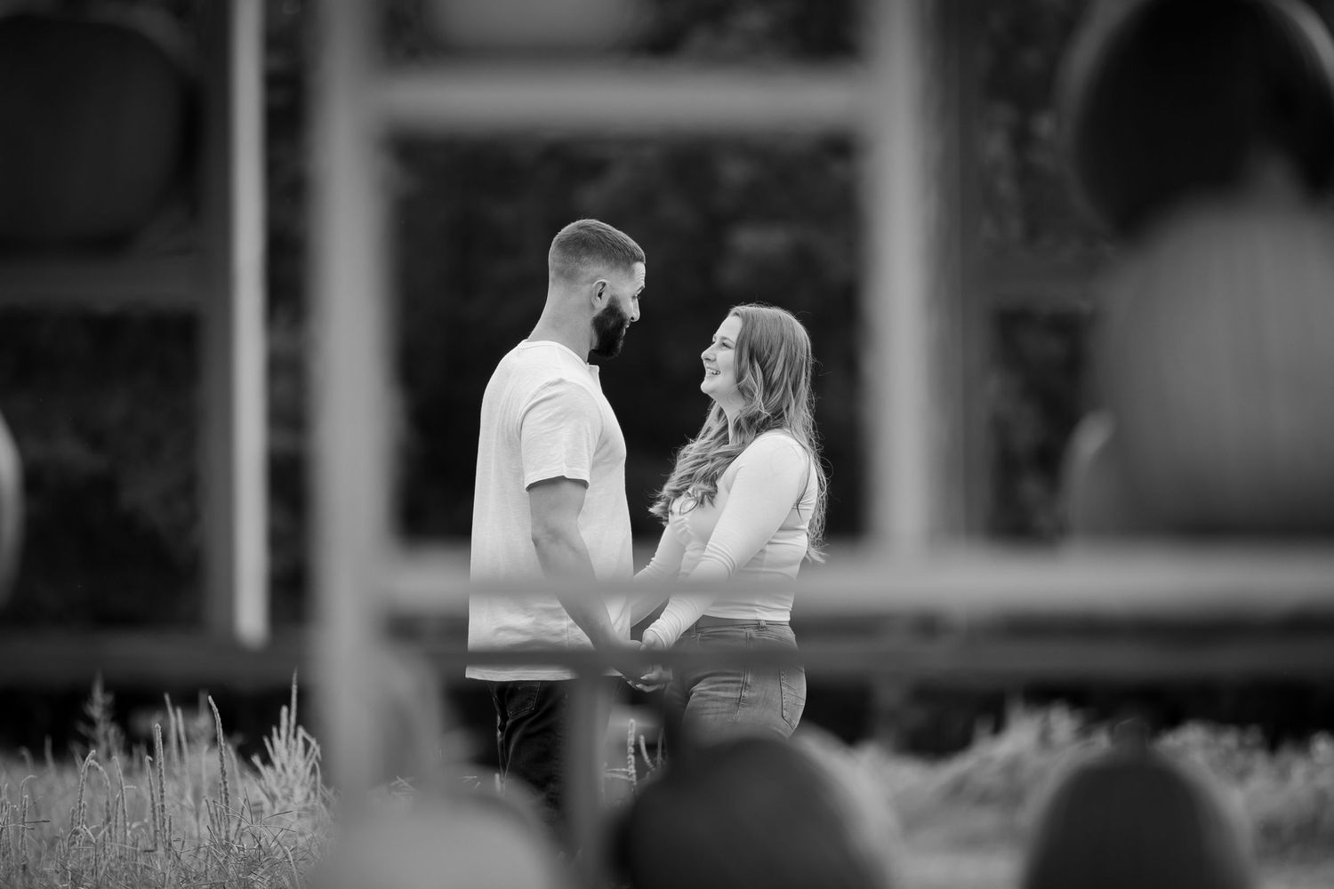 Black and white photo of a couple holding hands and gazing at each other outdoors near a winery.
