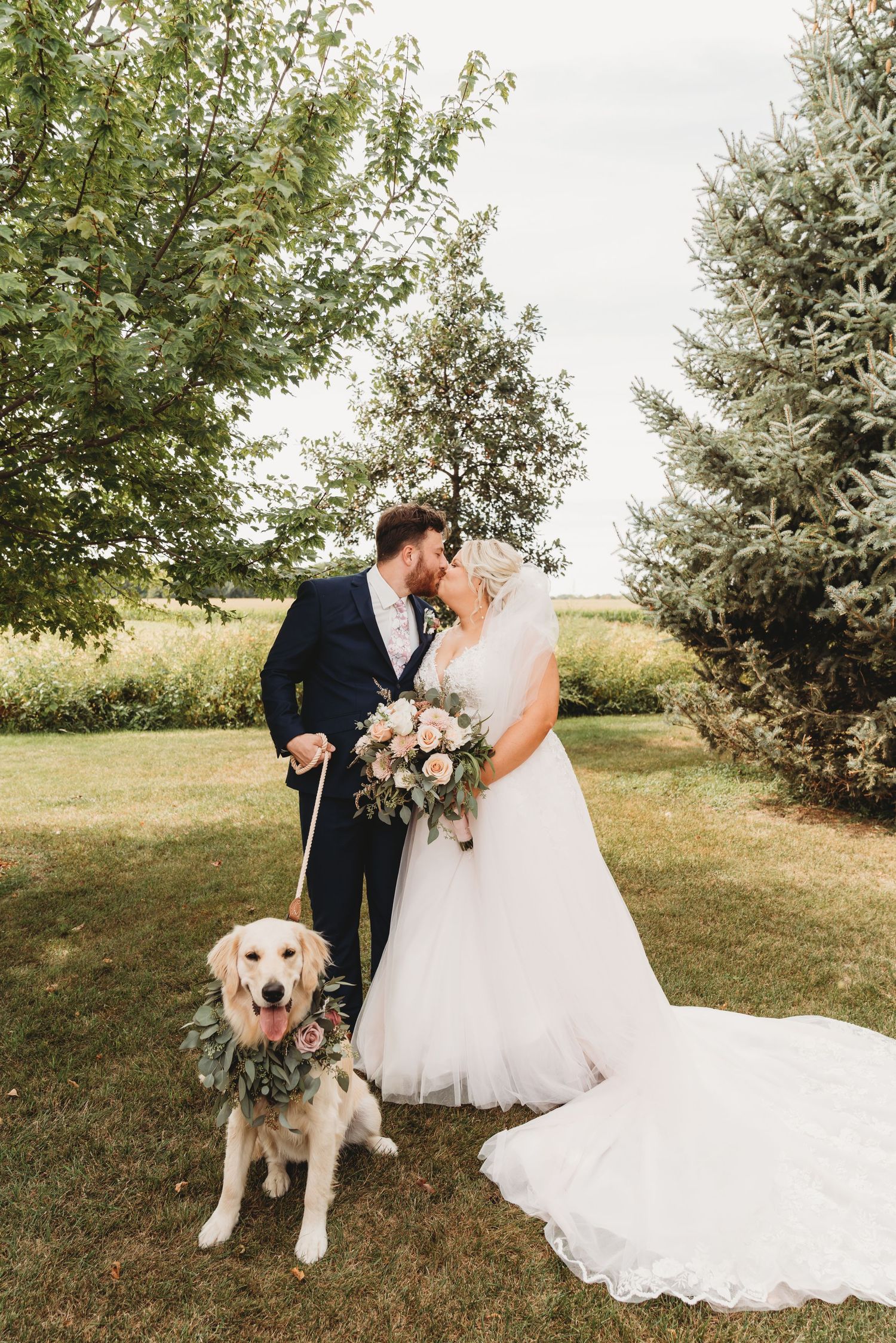 Beautiful outdoor wedding photo with couple and their golden retriever wearing floral collar.