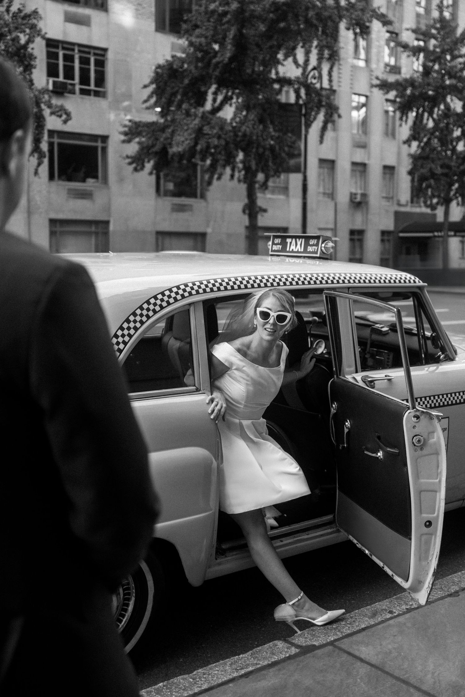 Bride in white dress and leather jacket poses with Eiffel Tower view in Paris.