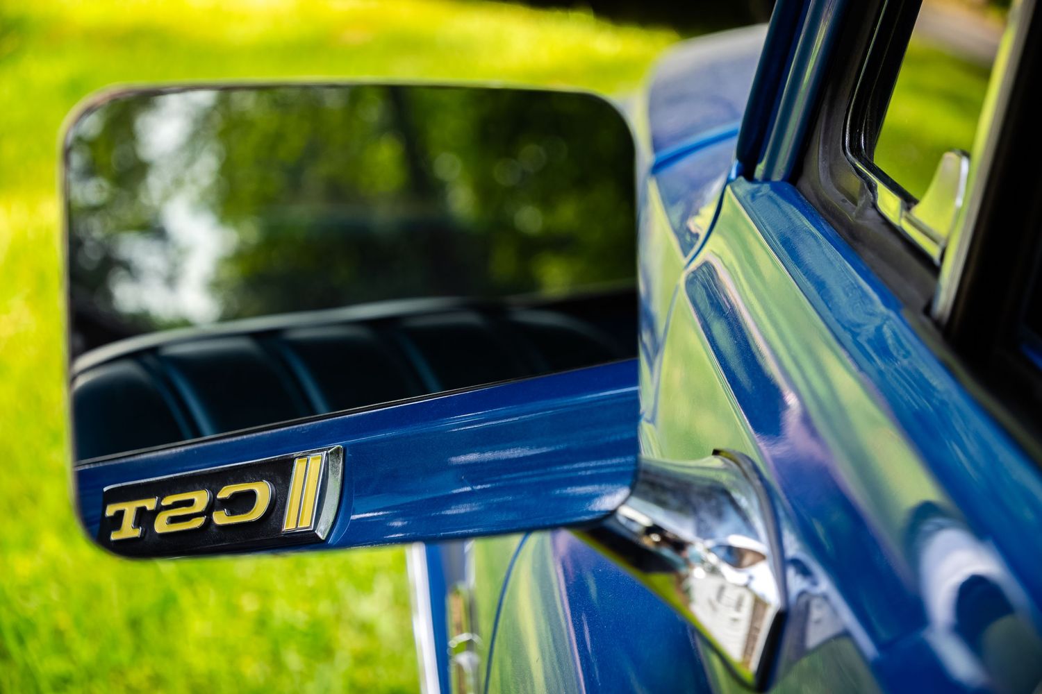 Close-up detail shot of a blue T20 badge on a sports car exterior with blurred green background.