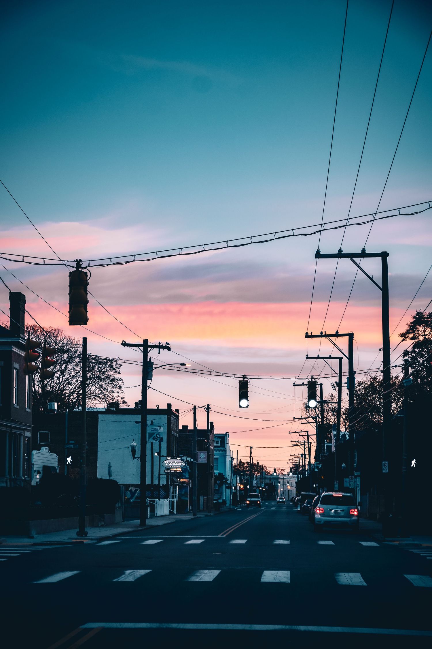 Urban street scene at dusk with silhouetted power lines against a vibrant pink and turquoise gradient sky.