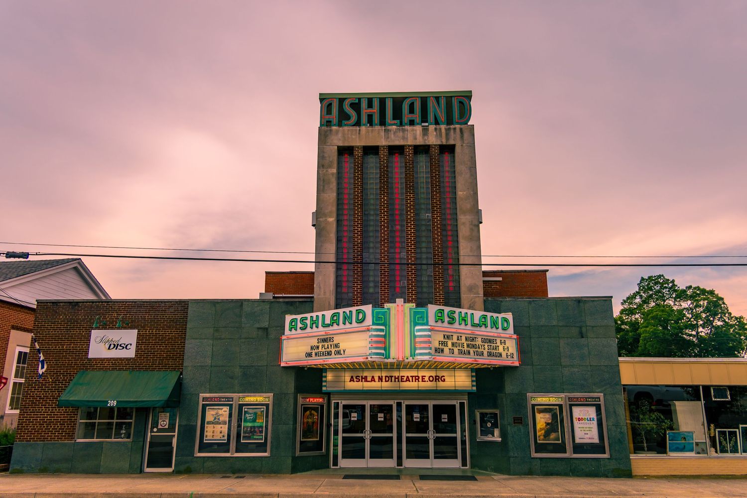 Historic Iroquois Theater with green facade and art deco signage glows under a dusky pink sky in small town America.
