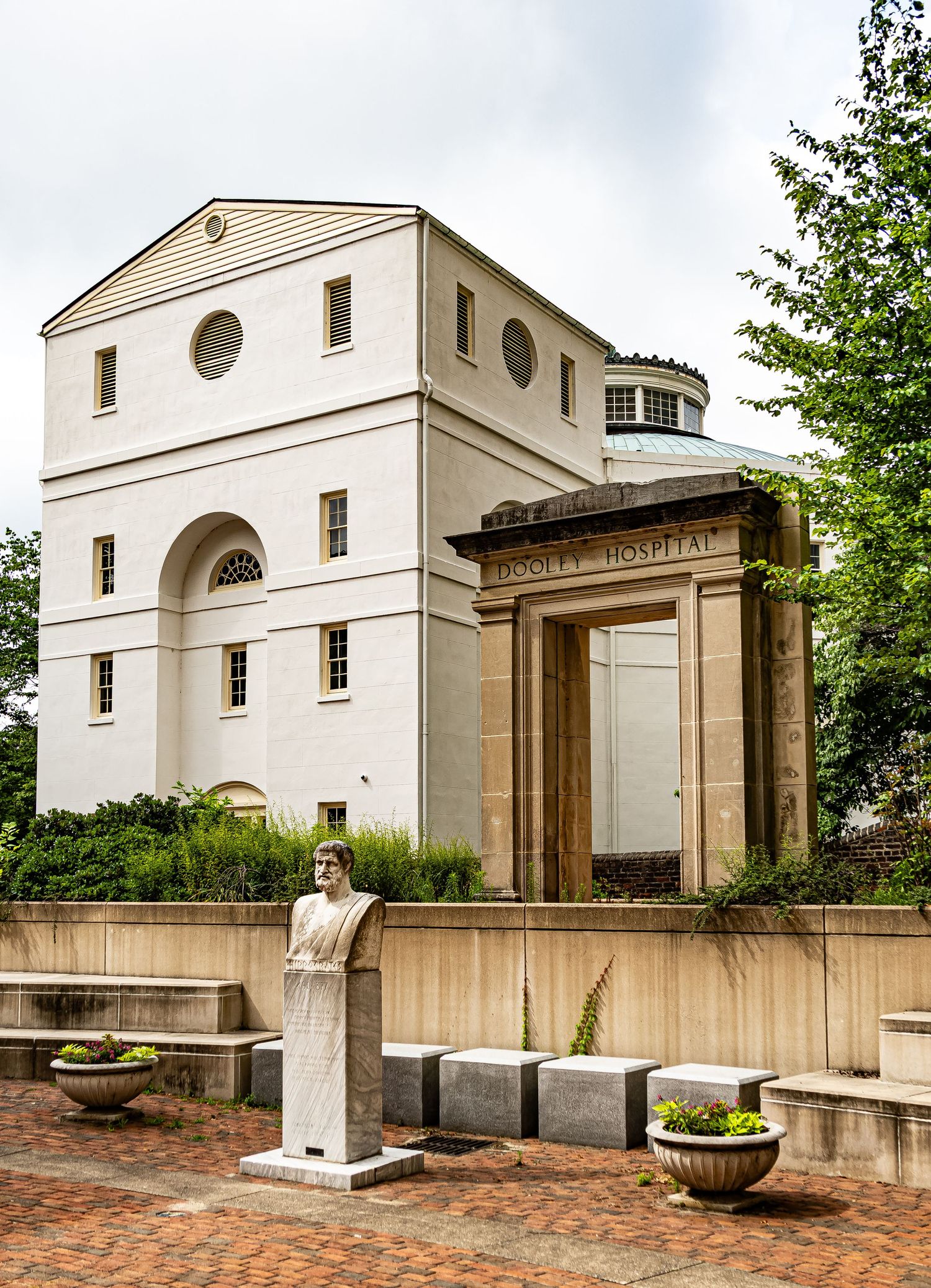 Neoclassical building with circular windows and stone facade featuring a columned entrance and decorative bust on display.