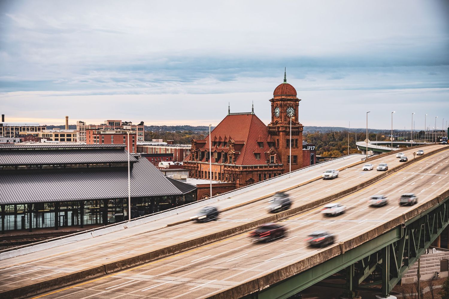 Historic brick train station with red roof and tower alongside elevated highway in Portland, Maine.