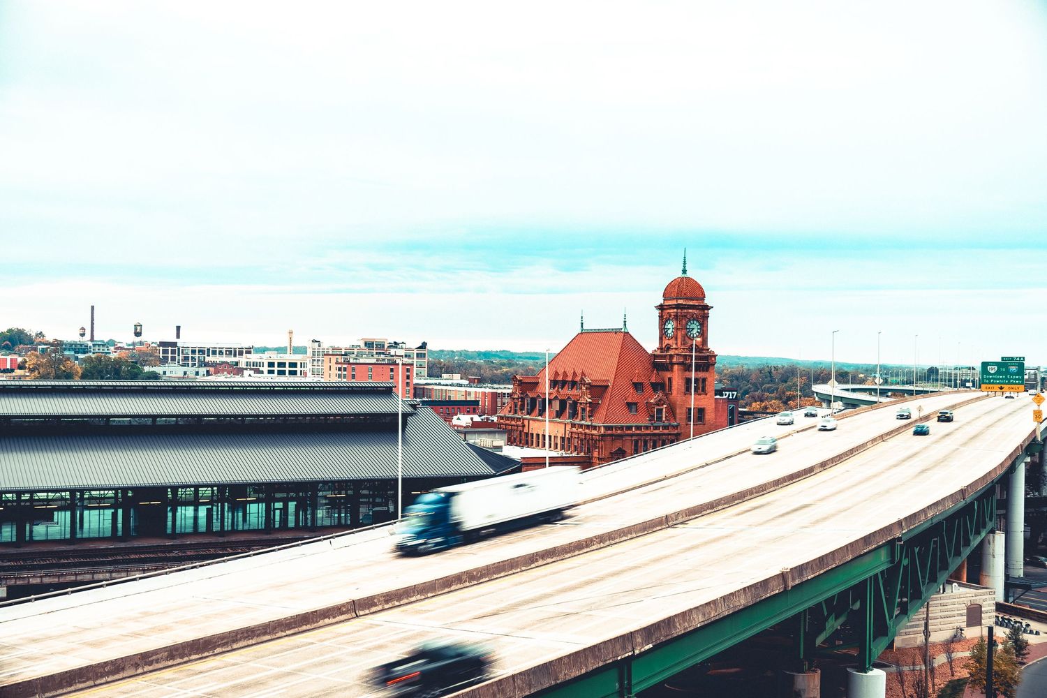 Panoramic view of a train station platform with curved tracks and red brick buildings in the background.