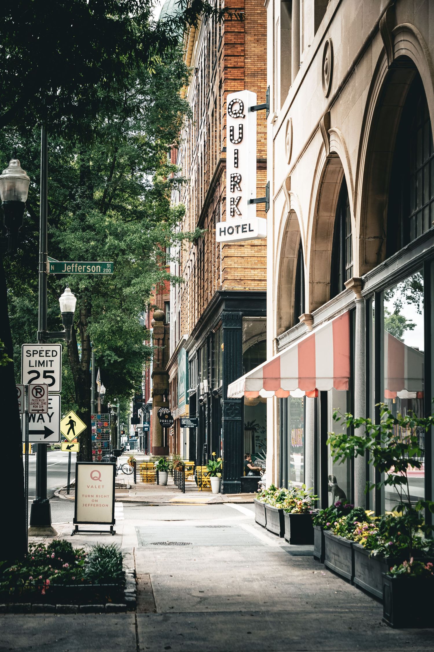 Architectural view of a historic brick building's arched colonnade with street lamps and planters along a quiet sidewalk.