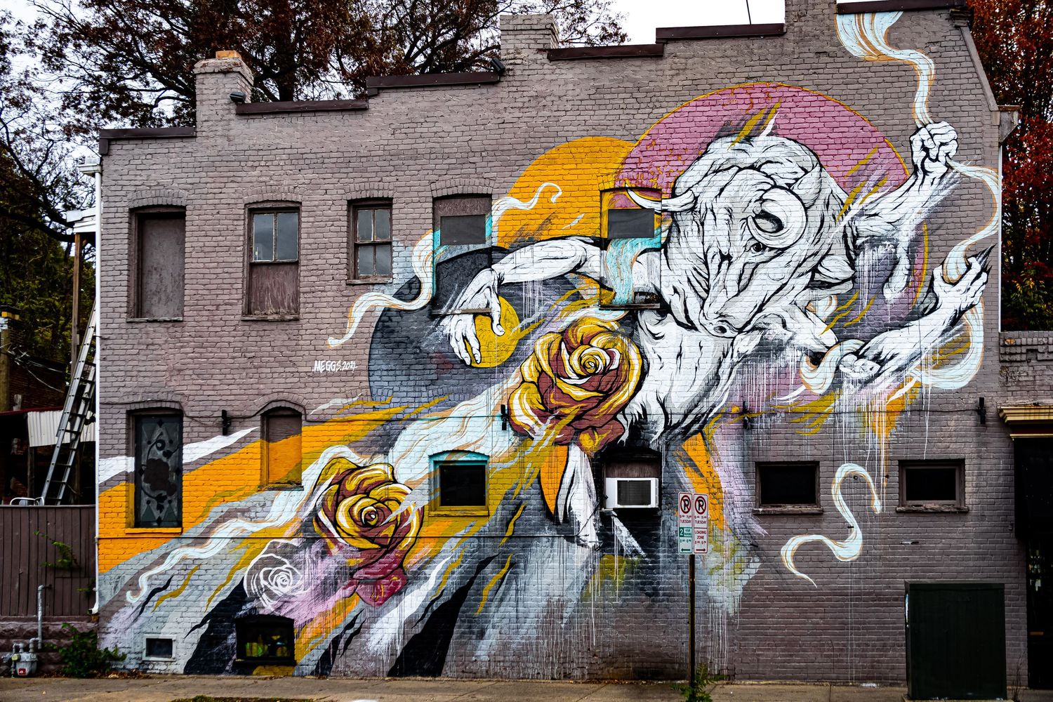 A large graffiti mural featuring abstract white and gold designs spans across a concrete wall in an urban setting.