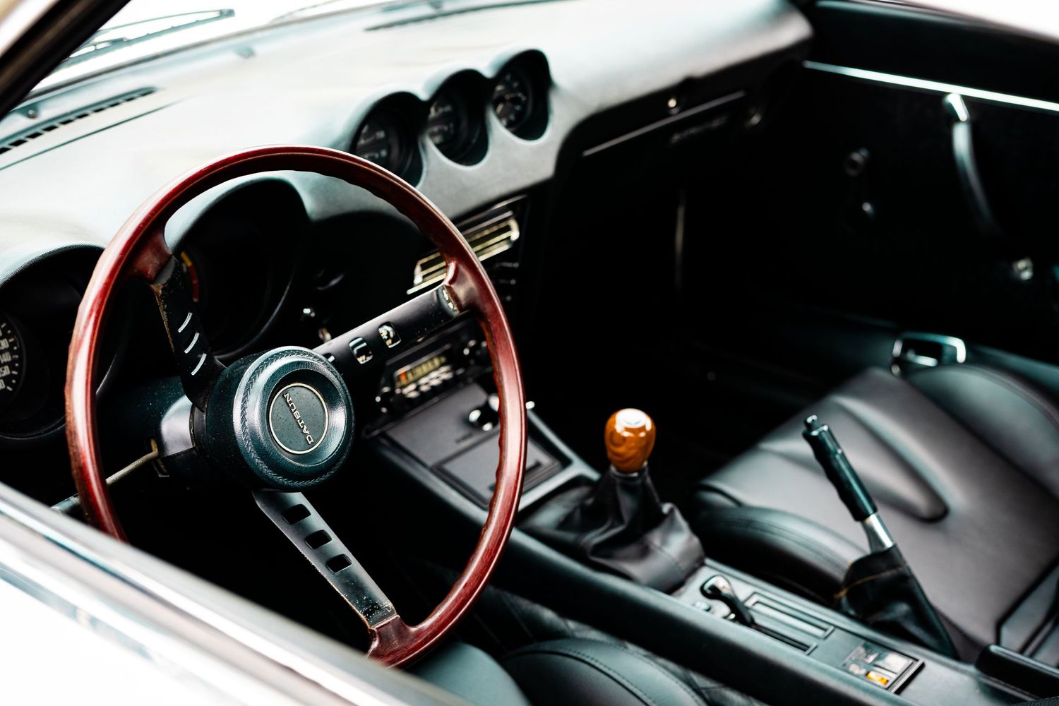 Close-up view of a black manual gear shift knob and leather boot in a classic car interior.