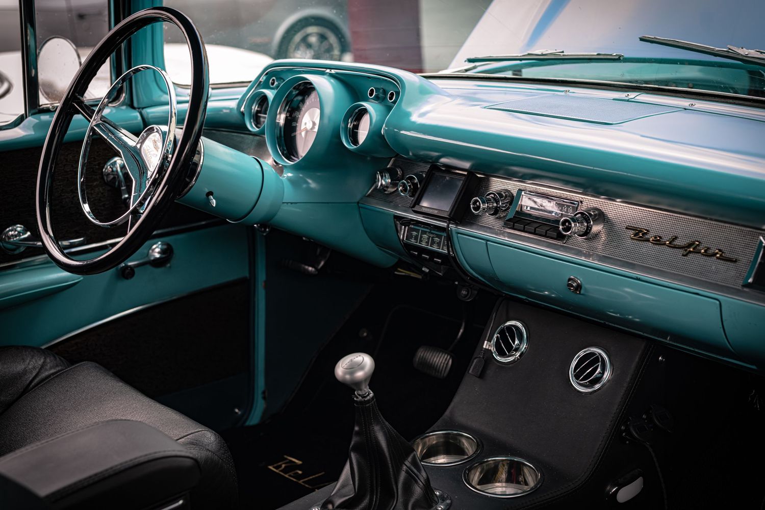 Vintage car interior details showing turquoise dashboard, steering wheel, and chrome accents in classic 1950s style.