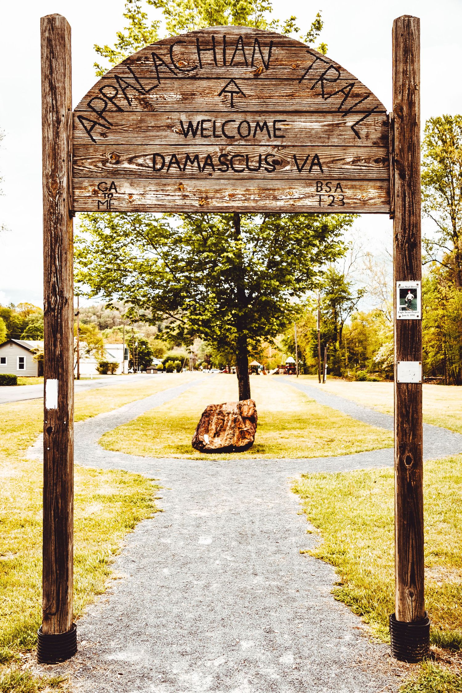 Rustic wooden welcome arch marks the entrance to Appalachian Trail with a gravel path leading through autumn scenery.
