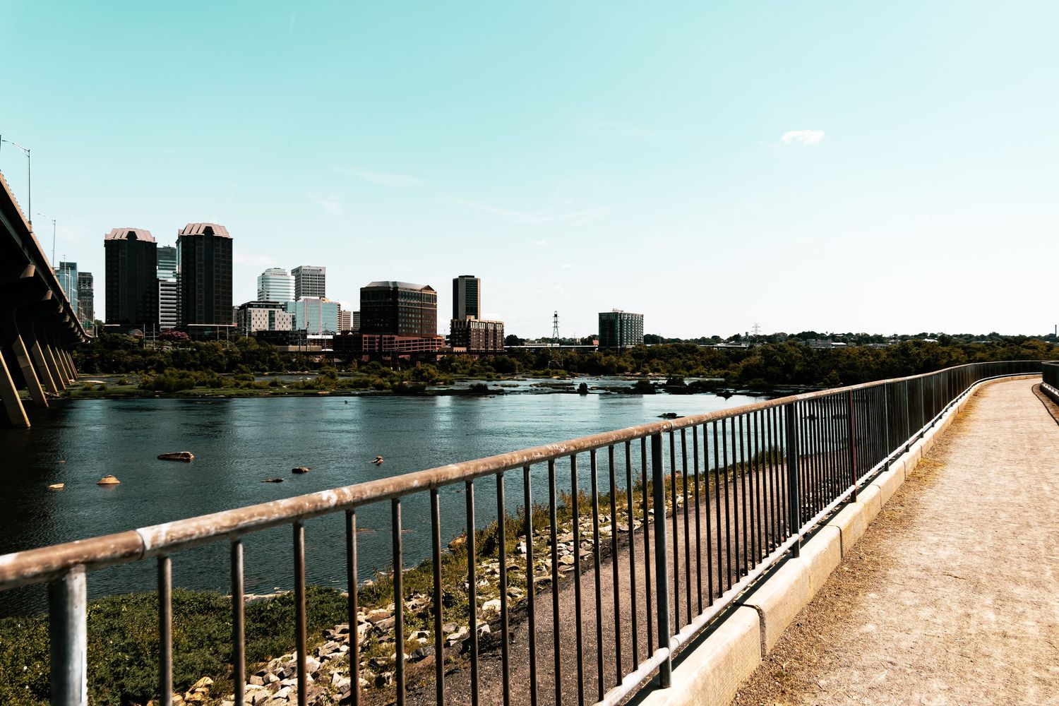 A panoramic series of photos showing a concrete walkway with metal railings along a waterfront with city skyline views.