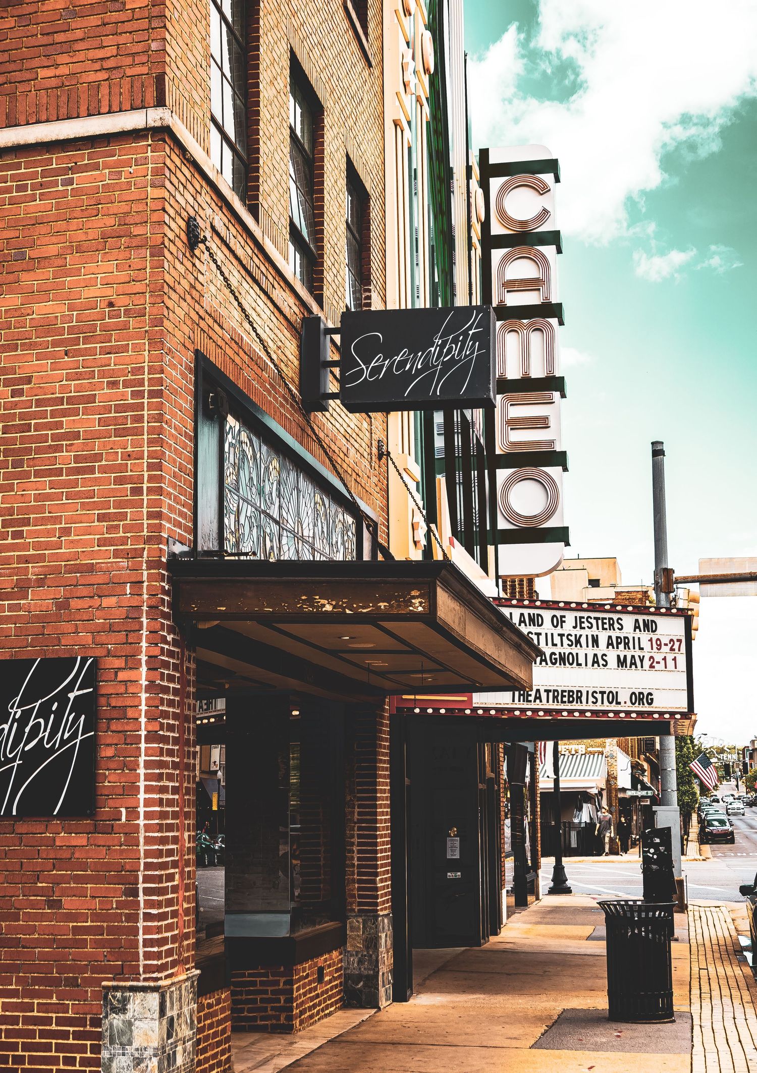 Exterior view of a brick storefront with black awnings and signage along a downtown sidewalk on a sunny day.