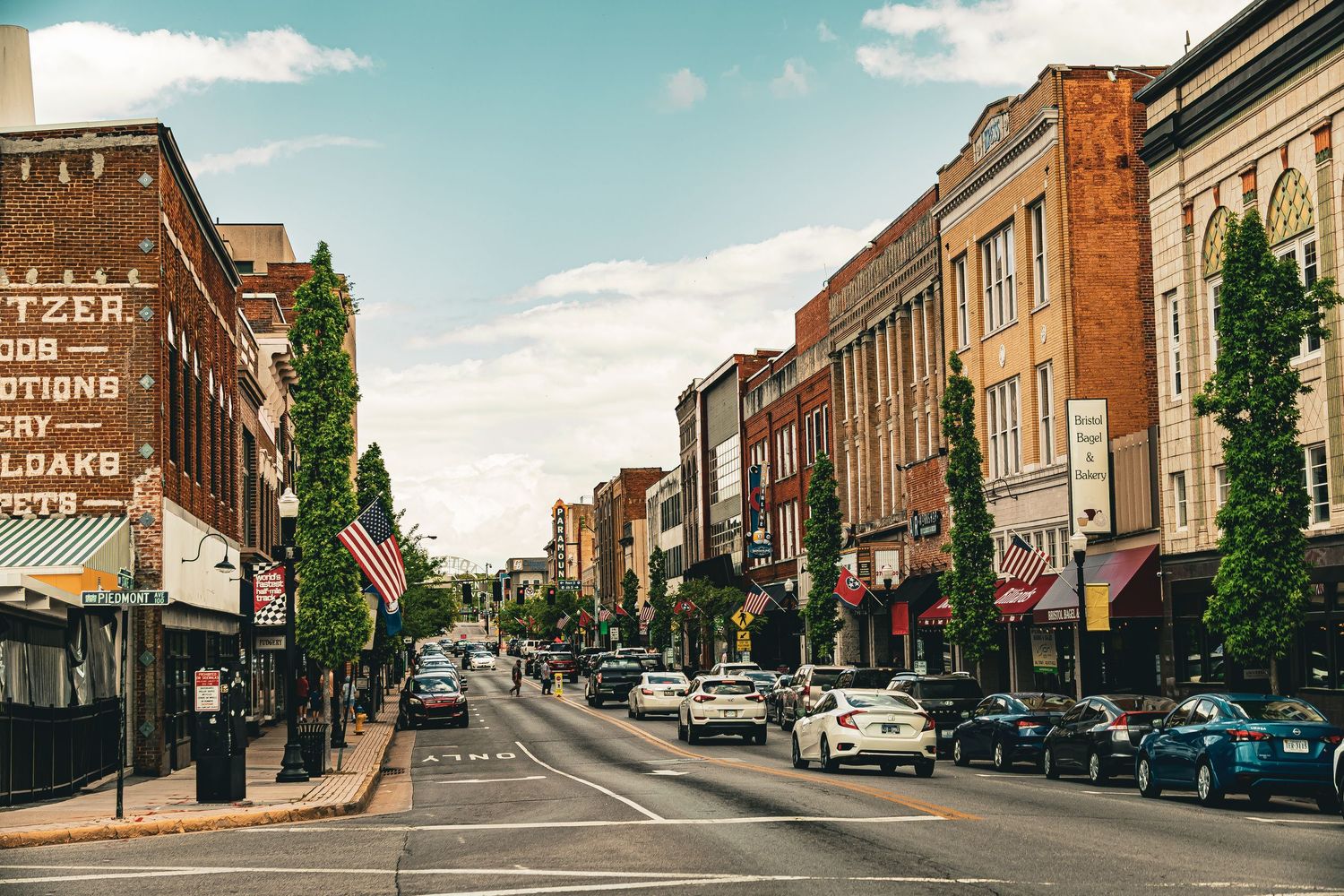 Historic brick buildings line both sides of a small town main street with parked cars and storefronts.