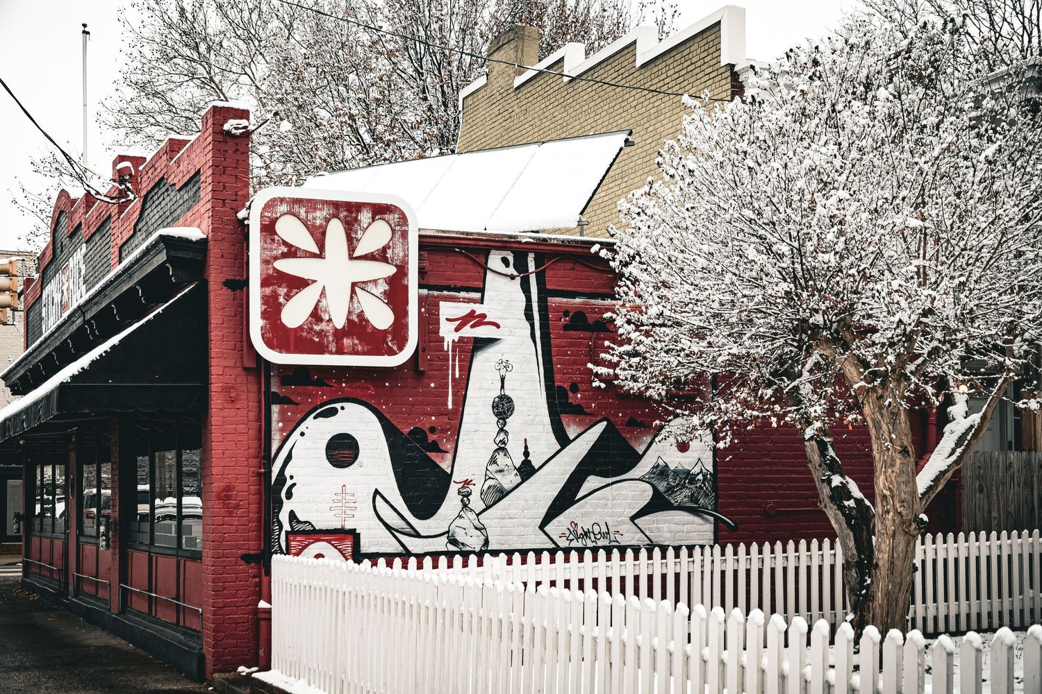 A vintage red train car sits on display behind a white picket fence in a snowy winter scene.