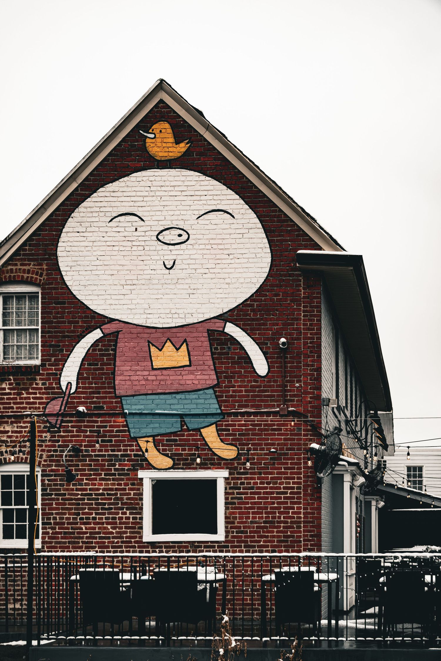 Whimsical cartoon character mural painted on brick building exterior showing three playful expressions.