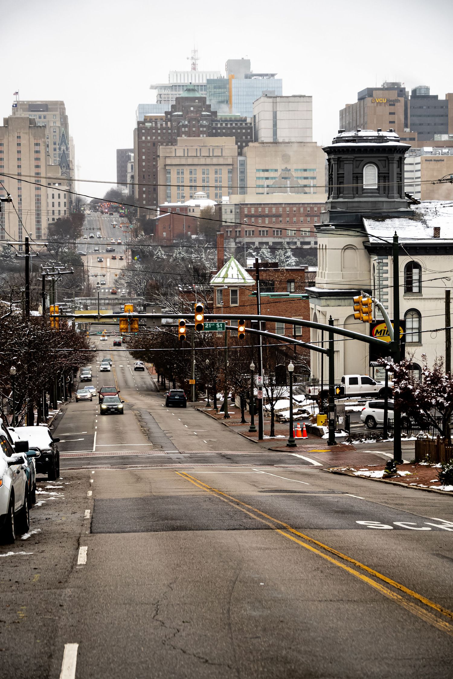 Urban street view of downtown Cincinnati with historic buildings, traffic lights and snow-dusted trees lining the road.