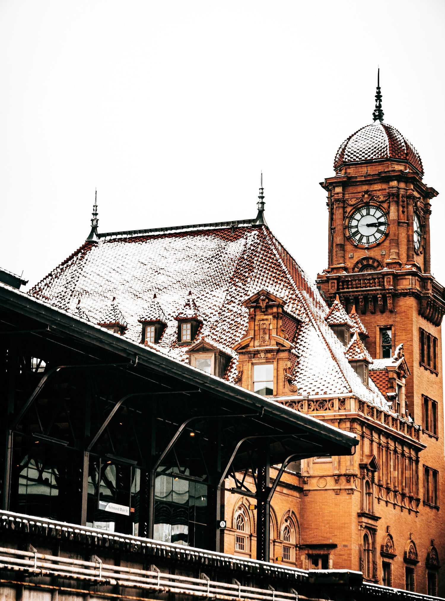 Historic Victorian railway station with ornate clock tower and snow-covered roof in warm sepia tones.