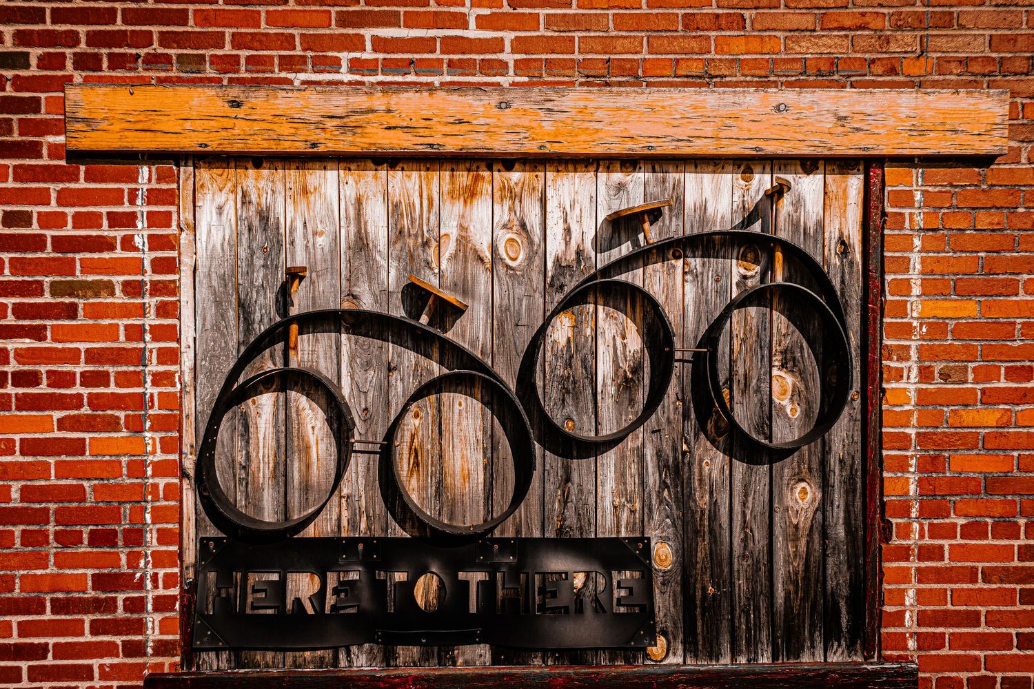 Rustic wooden door with bicycle art silhouette mounted on red brick wall features Here to Move text.