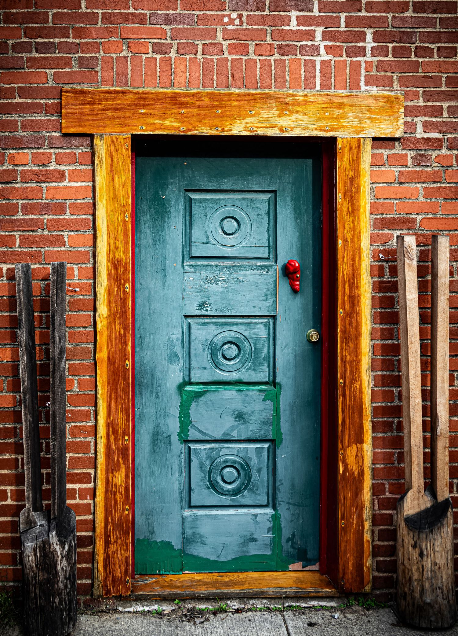 Panoramic view of three vintage turquoise doors with wooden frames set against a weathered red brick wall.
