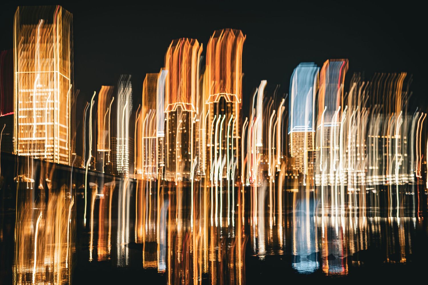 Abstract urban nightscape with vertical light streaks creating a blurred reflection effect in dark tones.