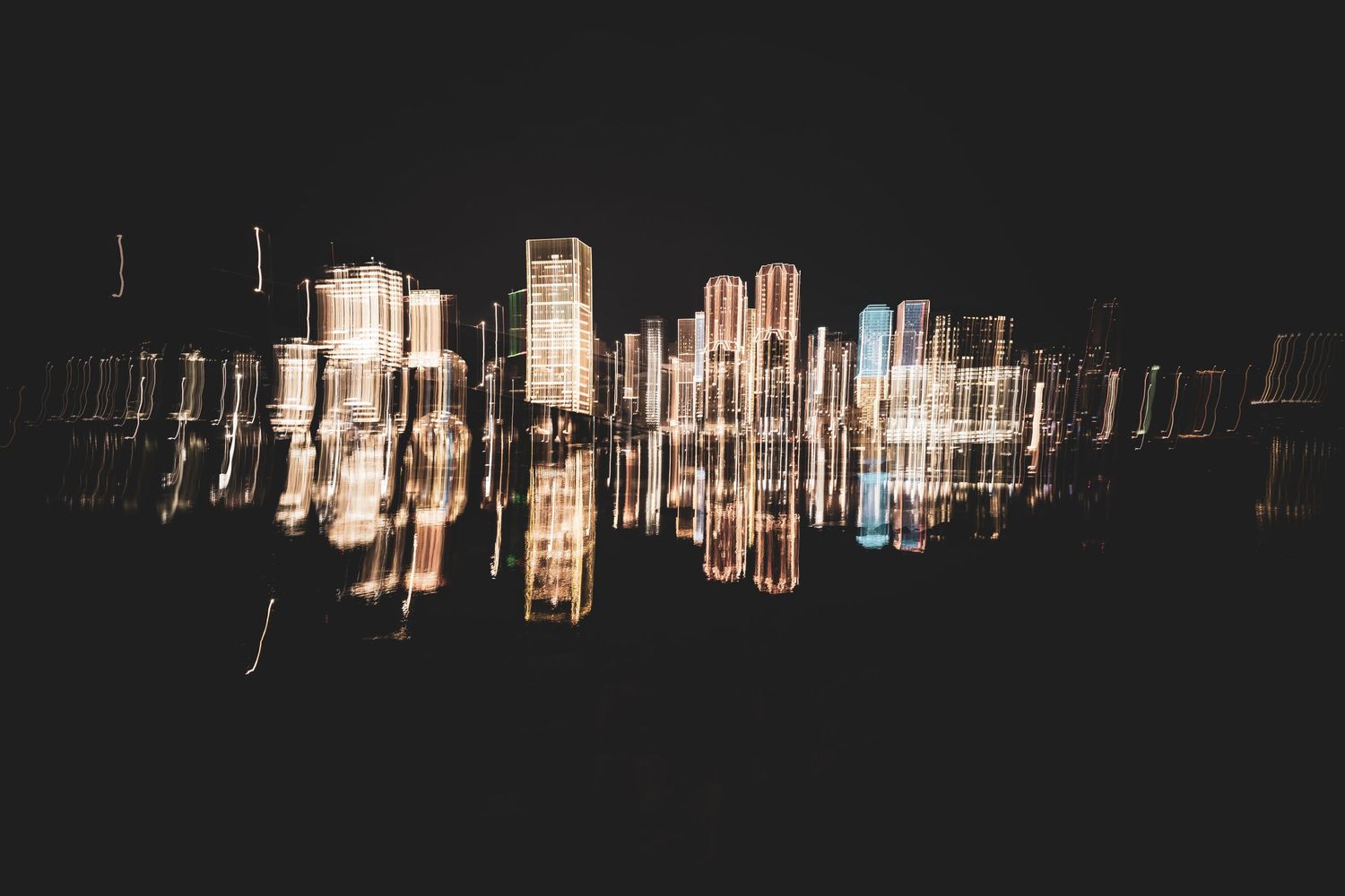 City skyline buildings reflected in calm water at night creating a mirror-like symmetrical pattern.