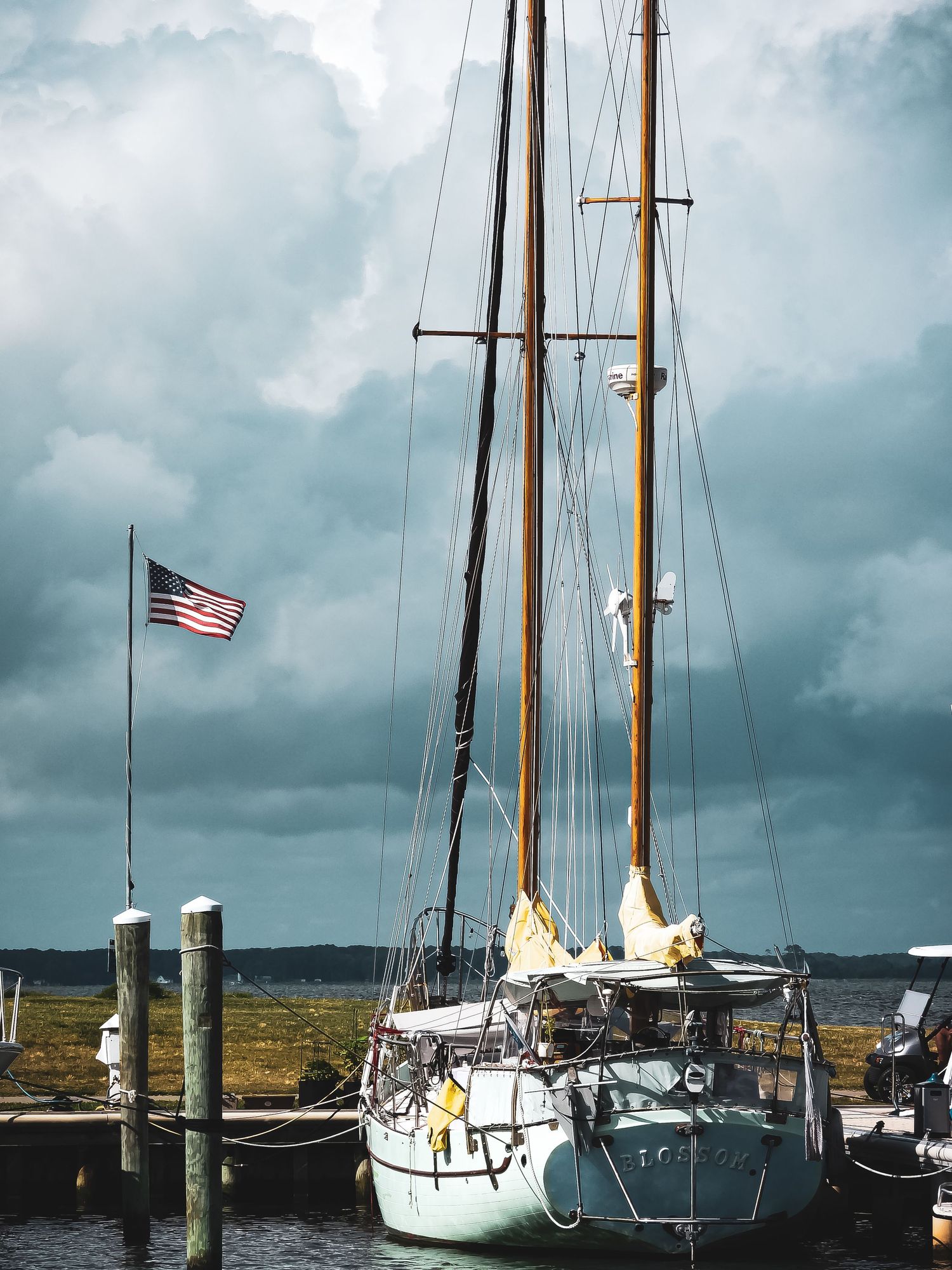Three sailboats docked at a marina under stormy skies with an American flag flying in the wind.