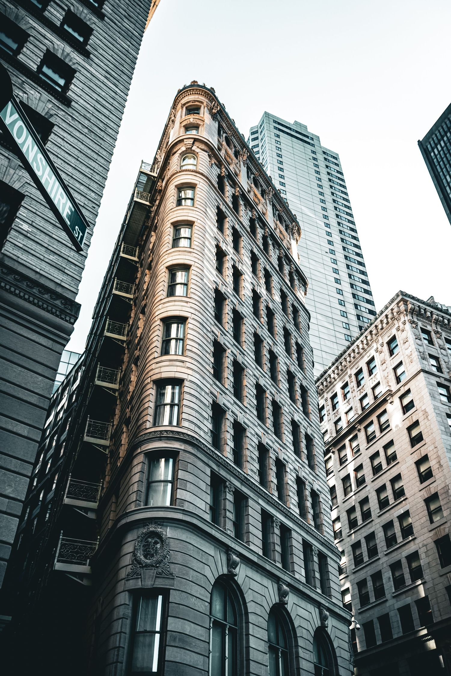 Historic Flatiron-style building with ornate facade stands among modern skyscrapers in downtown financial district.