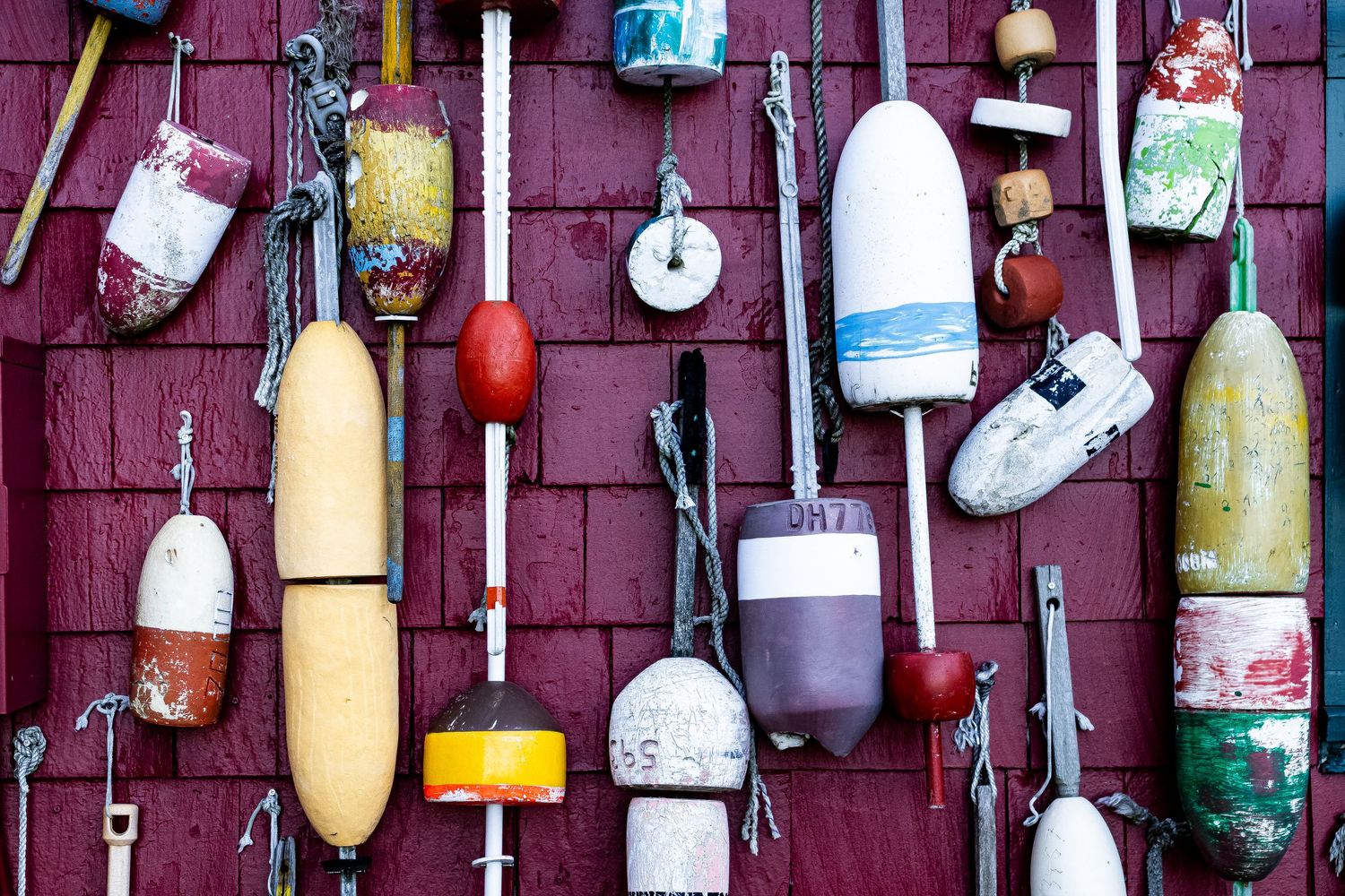 Colorful vintage buoys and floats hang on a weathered red wooden wall creating a nautical display.