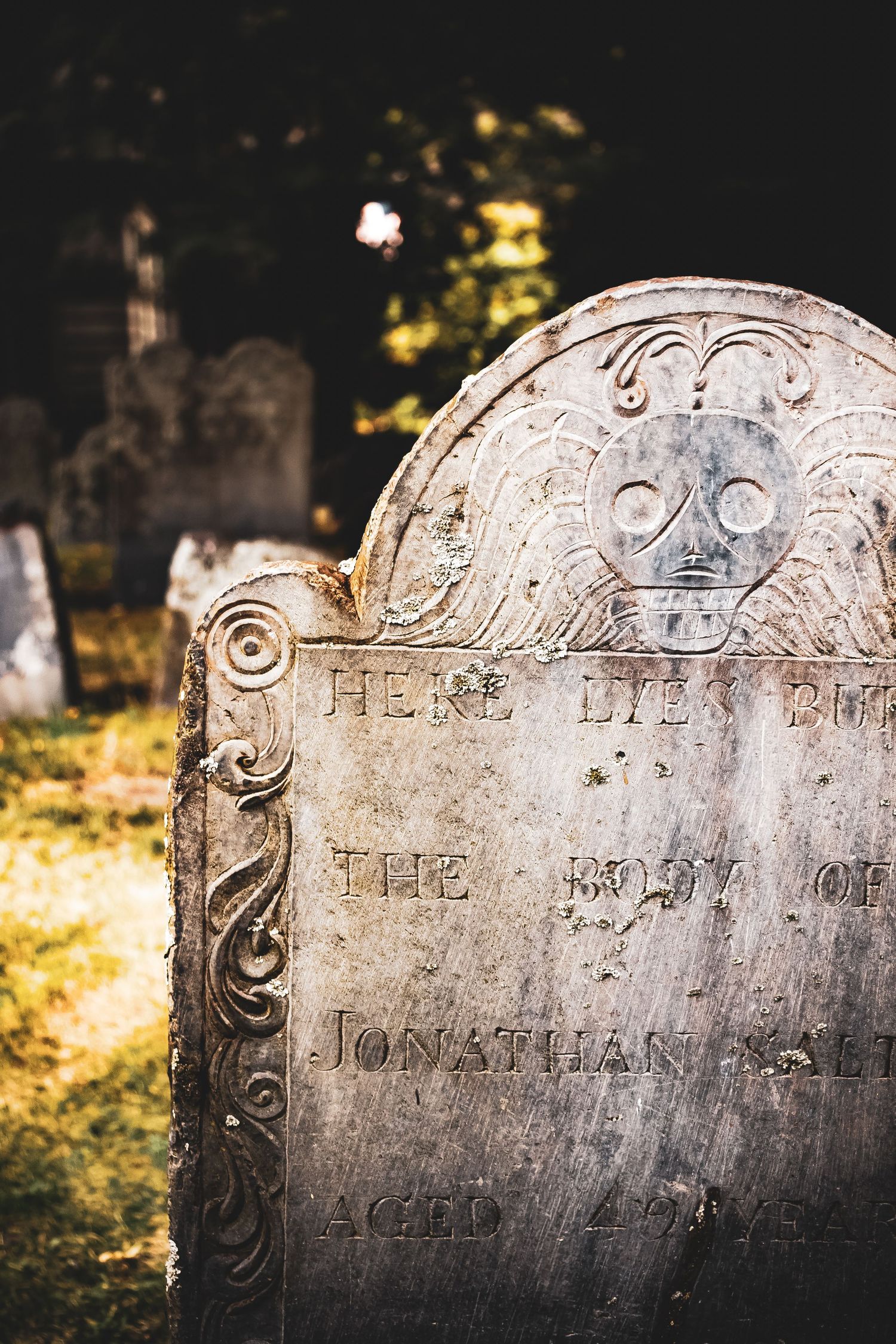 Close-up shots of weathered stone gravestones with ornate carvings and text in a historic cemetery during golden hour.