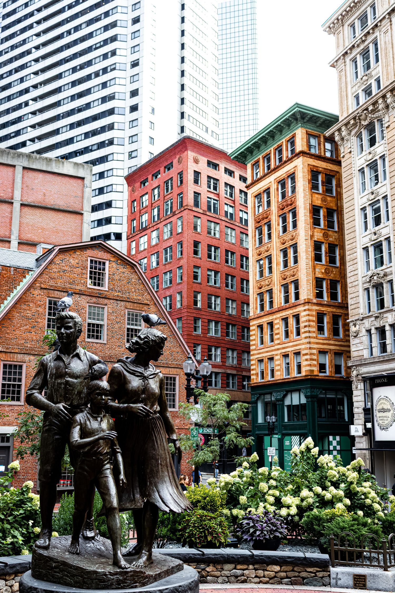 Bronze sculpture of two figures reading together in an urban garden surrounded by historic brick buildings in Boston.