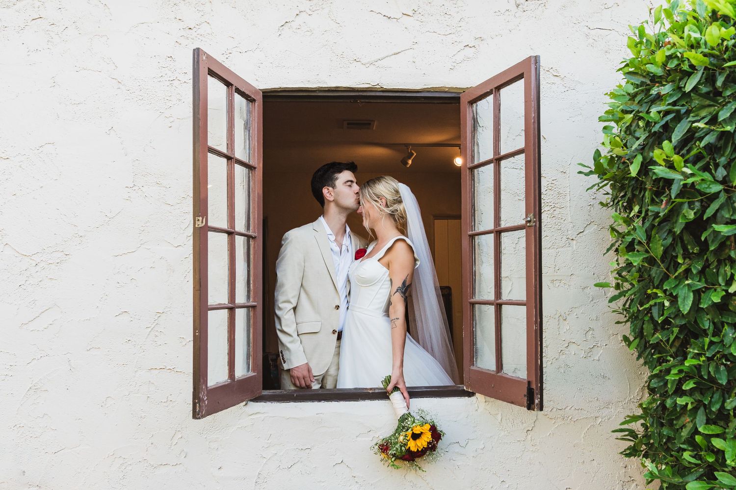 A couple poses together outdoors on their wedding day with the bride holding a white peony bouquet.