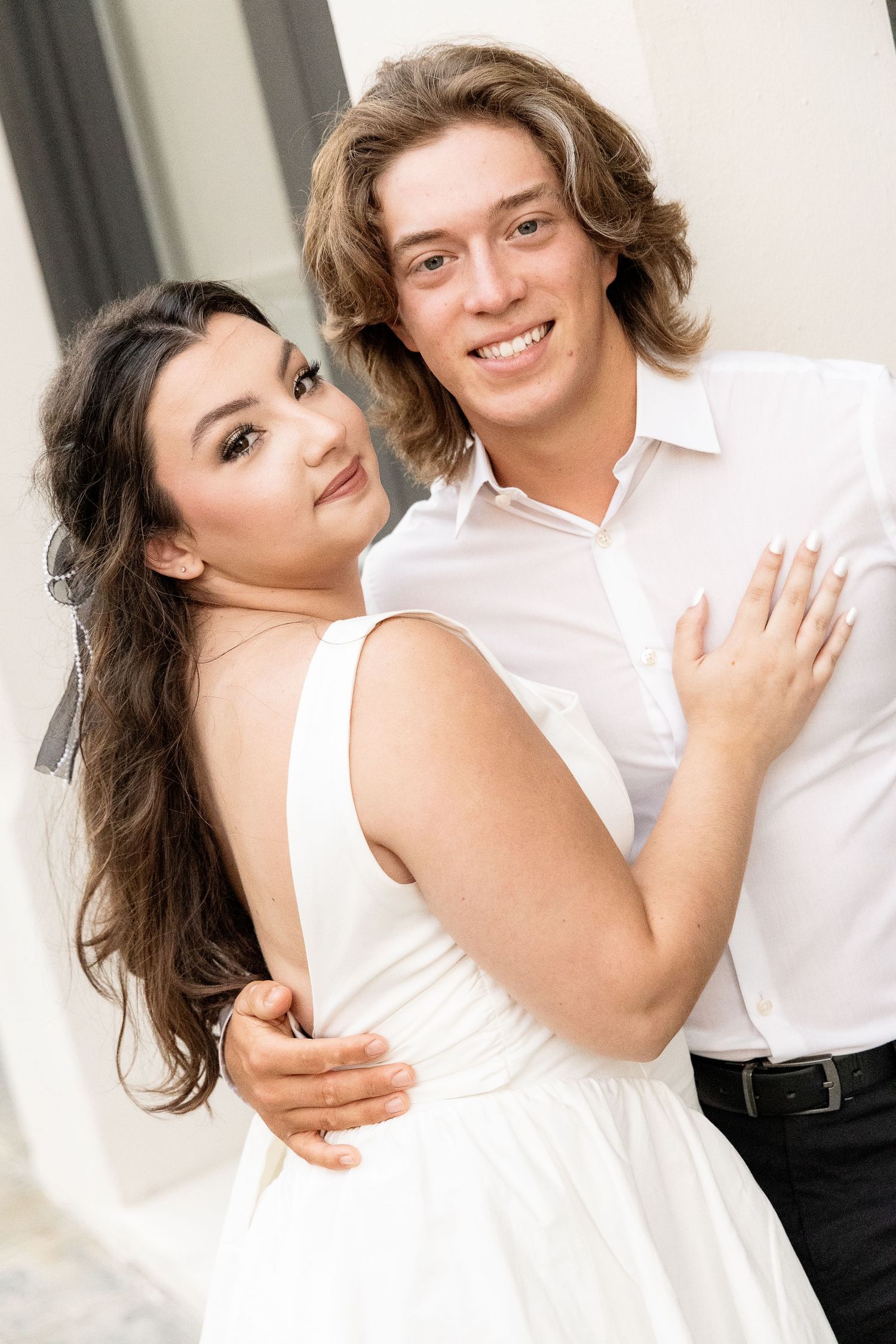 Couple in white and black formal wear posing together against white background.