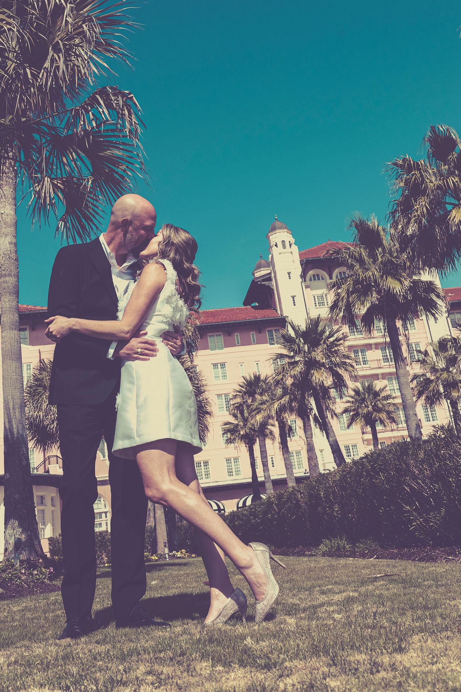 A sequence of four photos shows a couple embracing and spinning together on a grassy lawn with palm trees and buildings behind them.