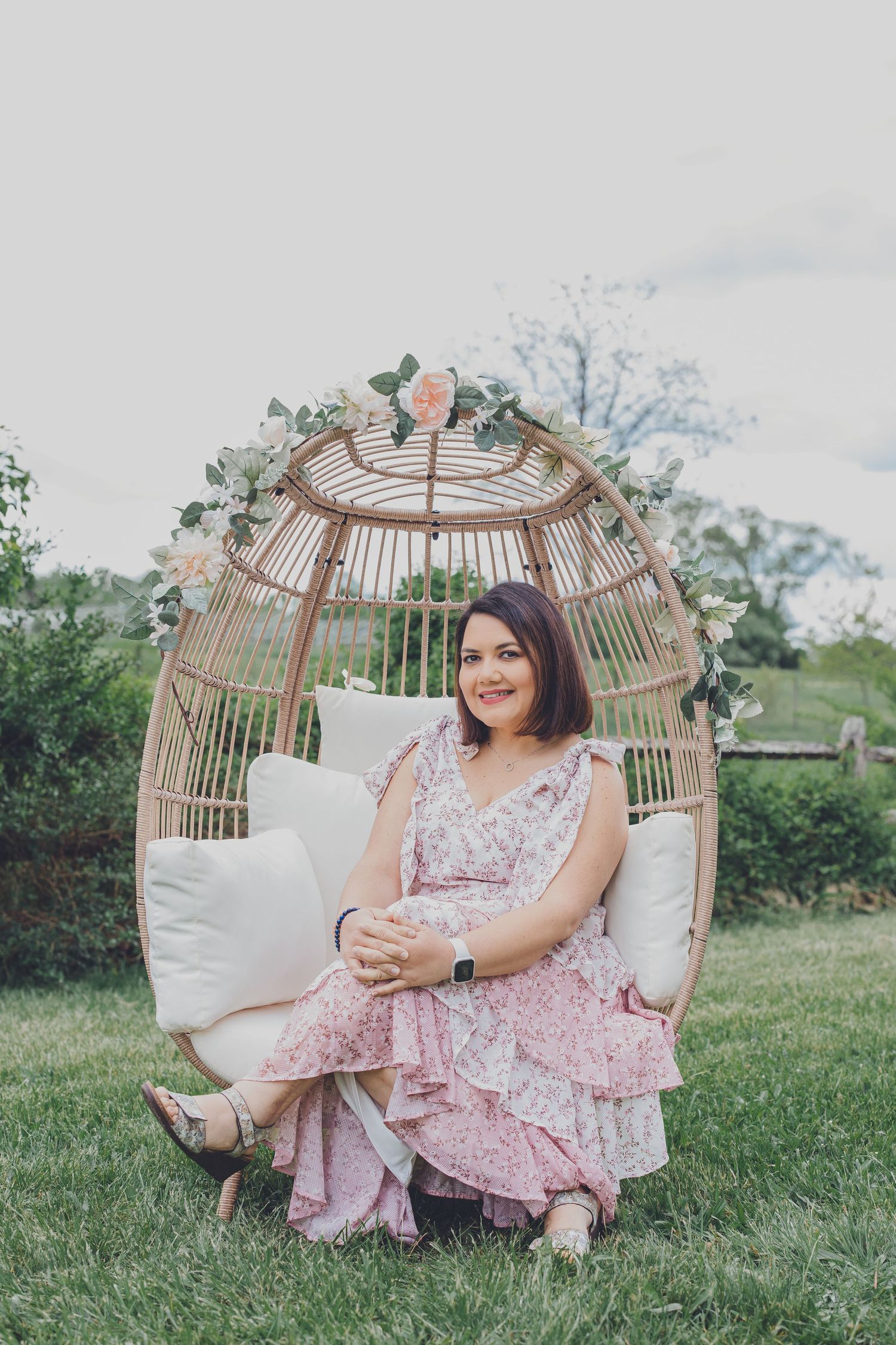 Portrait session in a wicker egg chair set in a garden with soft pastel tones.