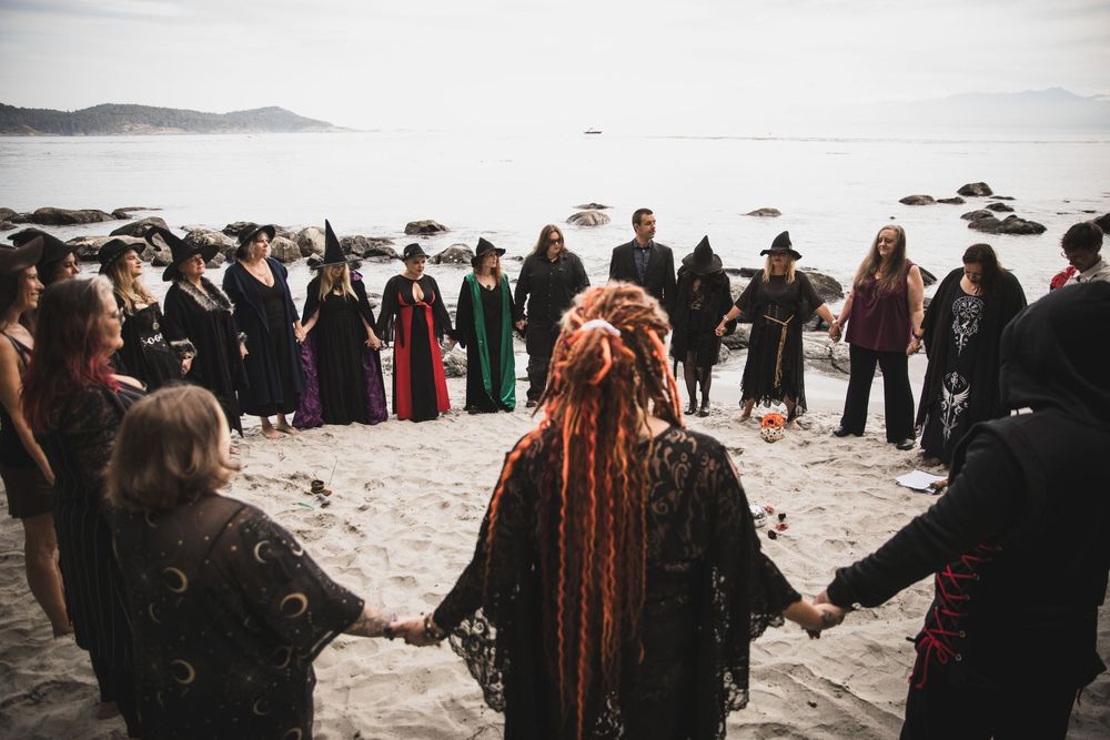 A group of people dressed in black gather on a scenic beach for a seaside ceremony at sunset.