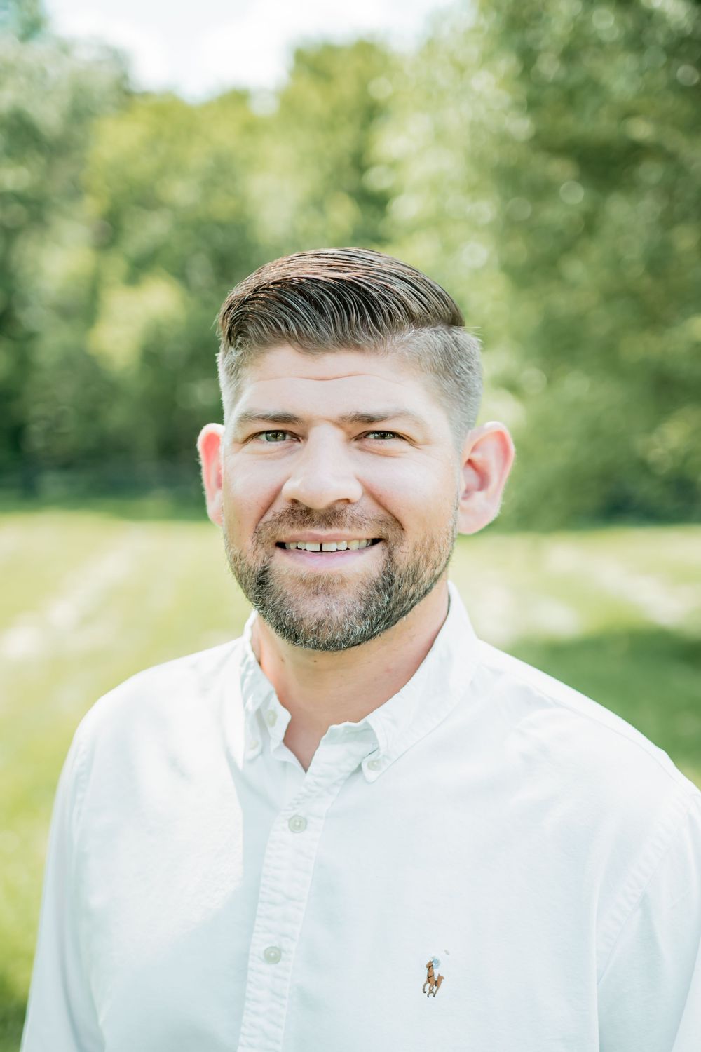 Professional headshots of someone wearing a white button-down shirt outdoors with green foliage in background.