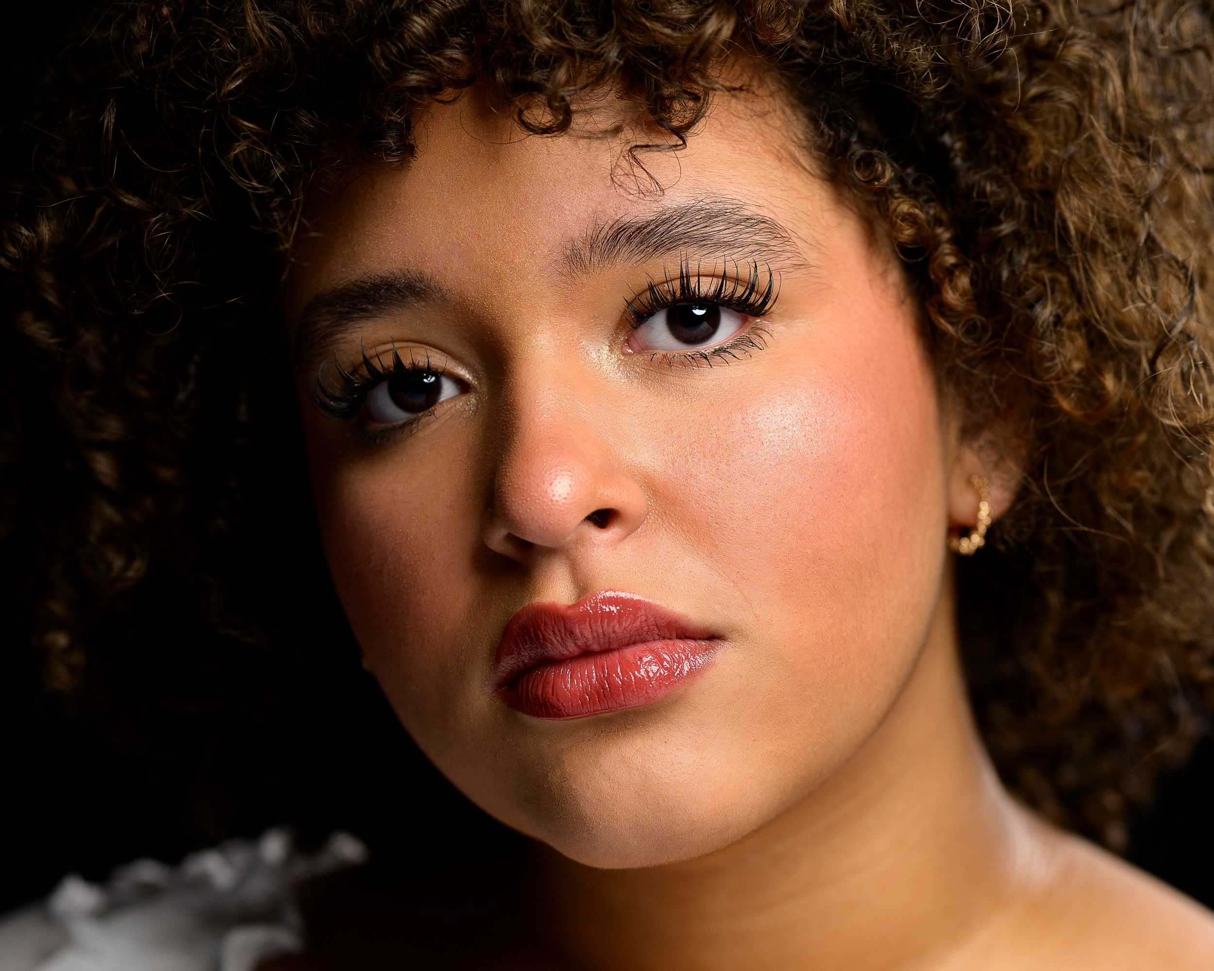 Close-up portrait of a young woman with curly hair and bold red lips gazing forward.