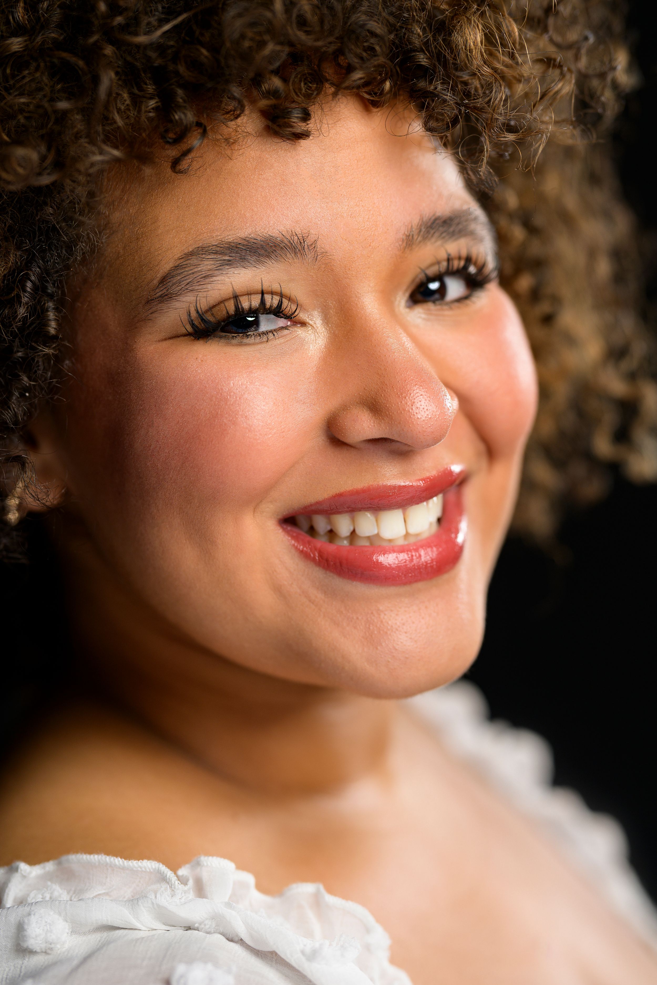 Close-up portrait of a smiling young woman with curly hair and red lipstick.