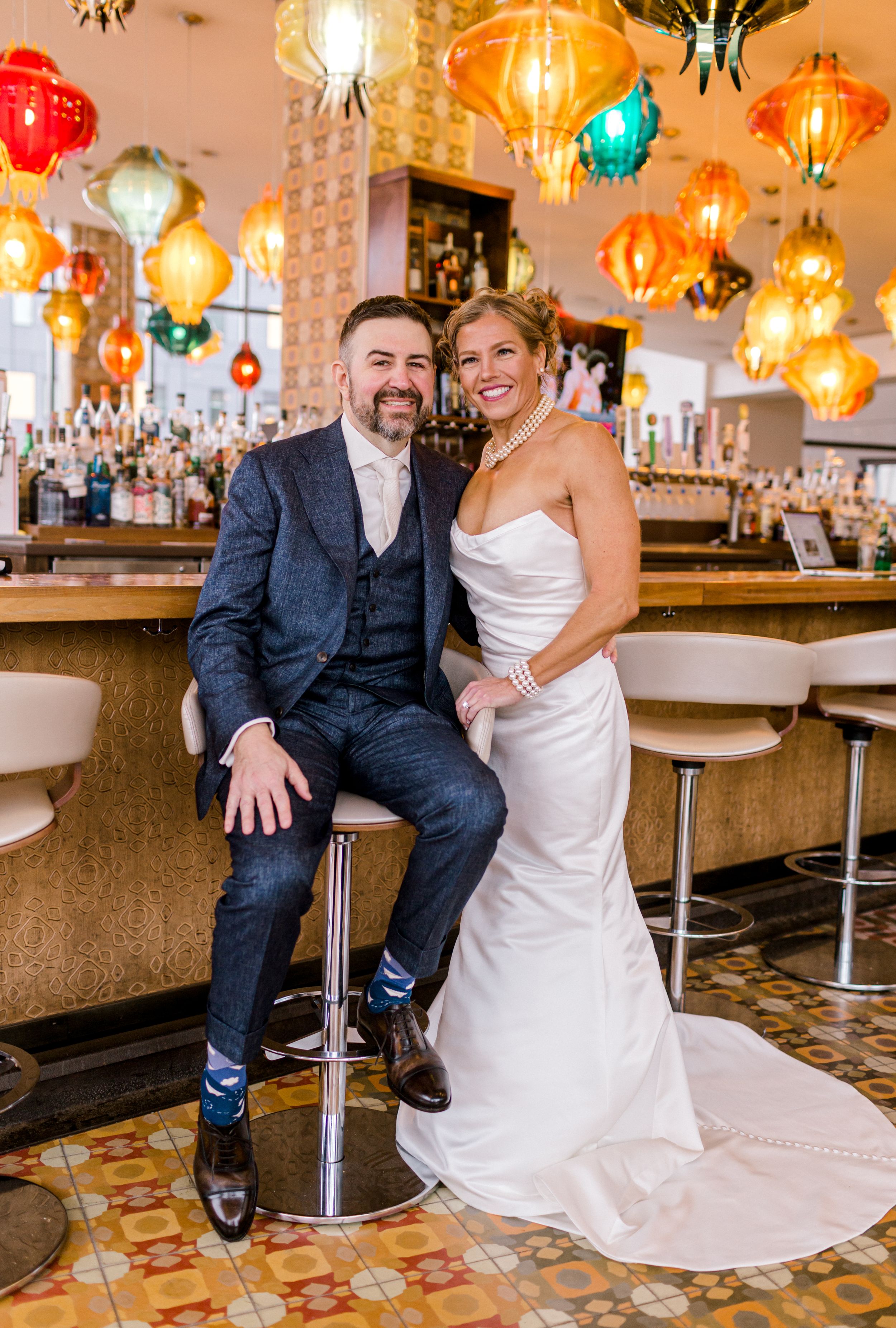 Bride and groom posing together at colorful bar venue with decorative hanging lanterns overhead.