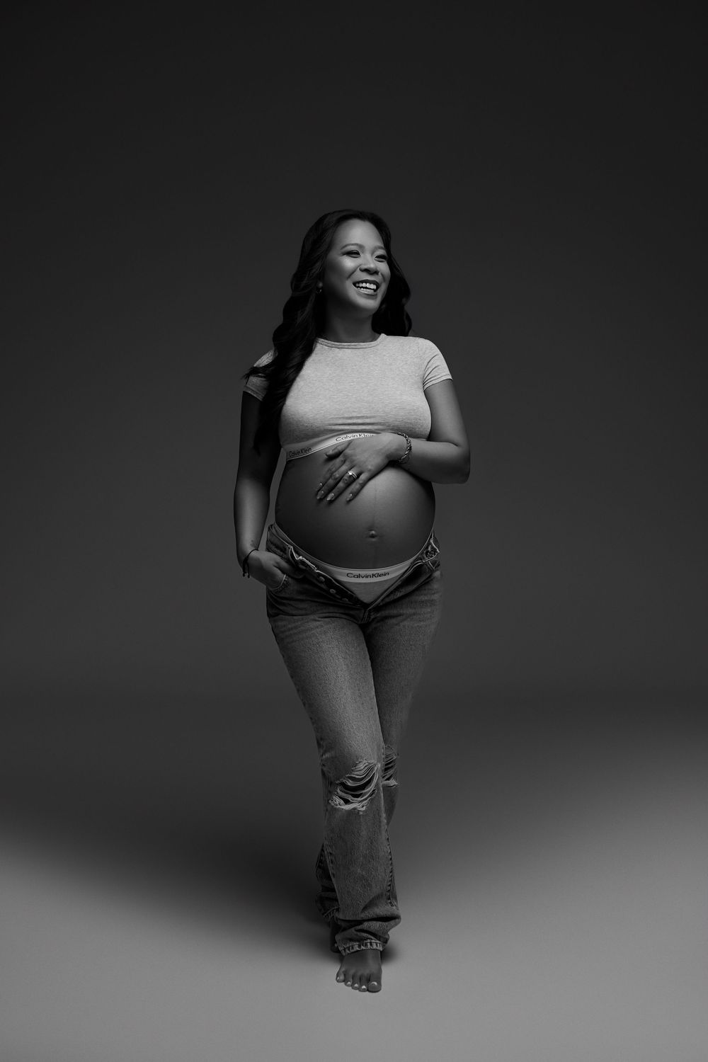 Black and white maternity photos showing a pregnant woman posing in casual clothing against a dark background. NJ maternity photographer