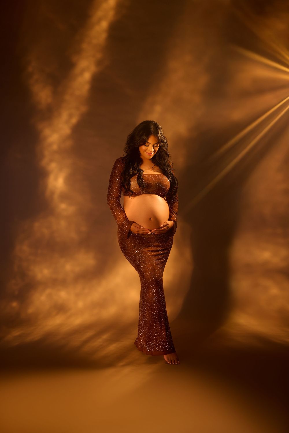 A figure in a dark dress poses dramatically against a warm sepia-toned background with dramatic lighting effects. brown maternity photos