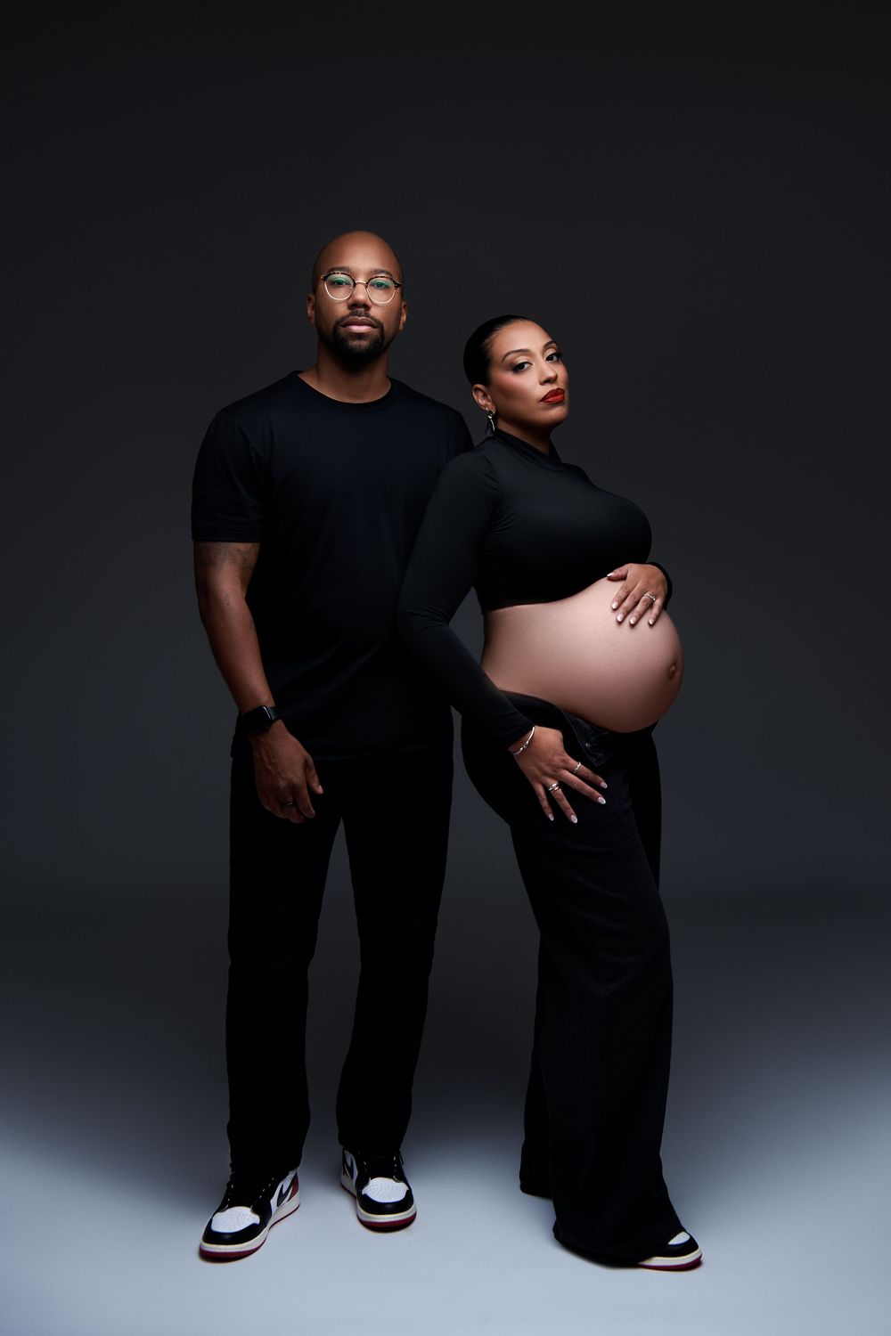Creative maternity photo series showing couple in black outfits against dark backdrop in minimalist style. NJ maternity photoshoot