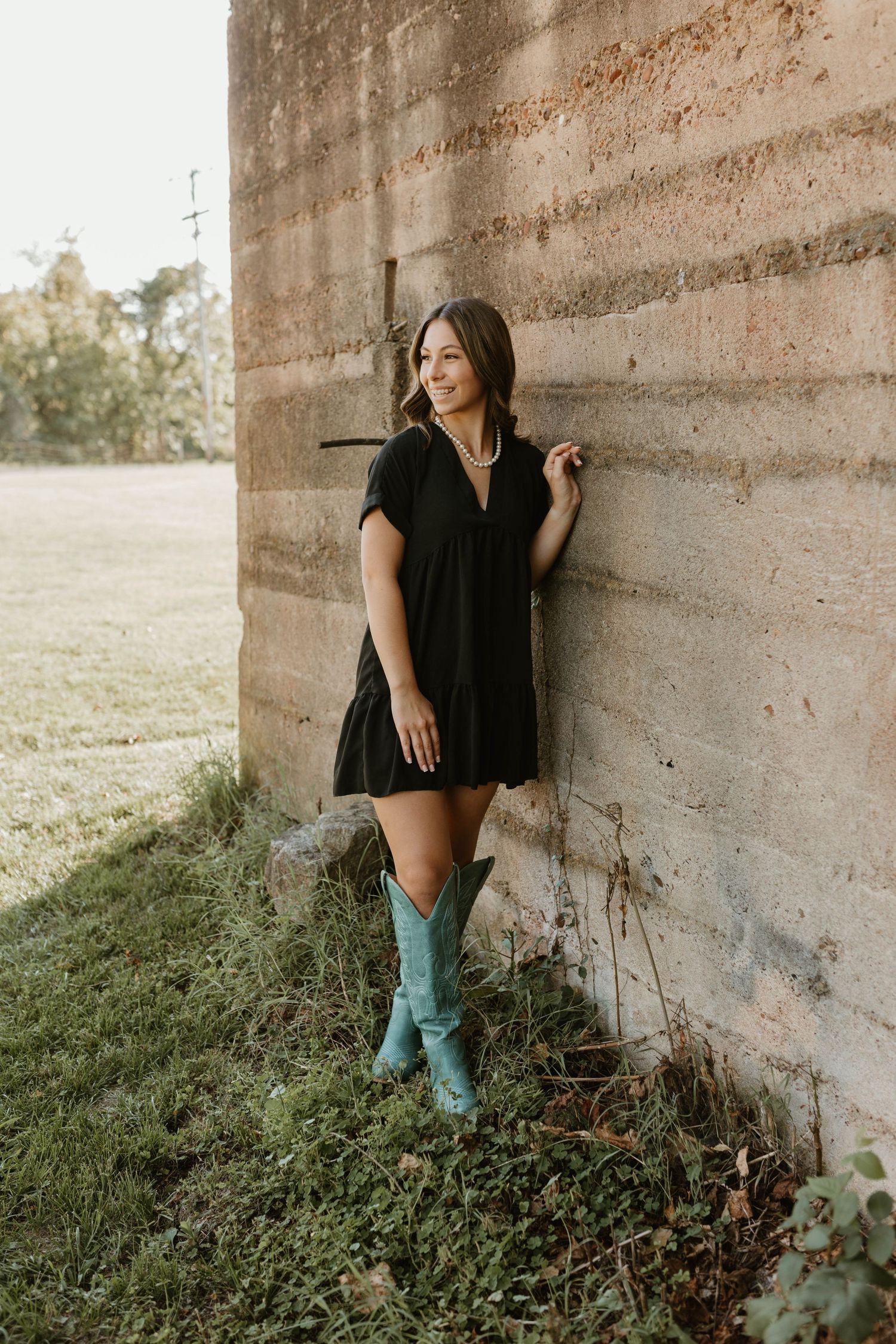 Artistic portrait series of woman in black top and blue jeans against rustic concrete wall.