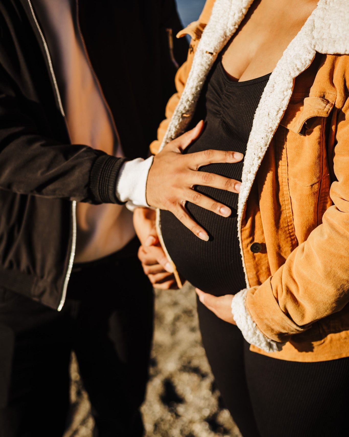 Close-up shot of hands touching a pregnant belly in golden sunlight.