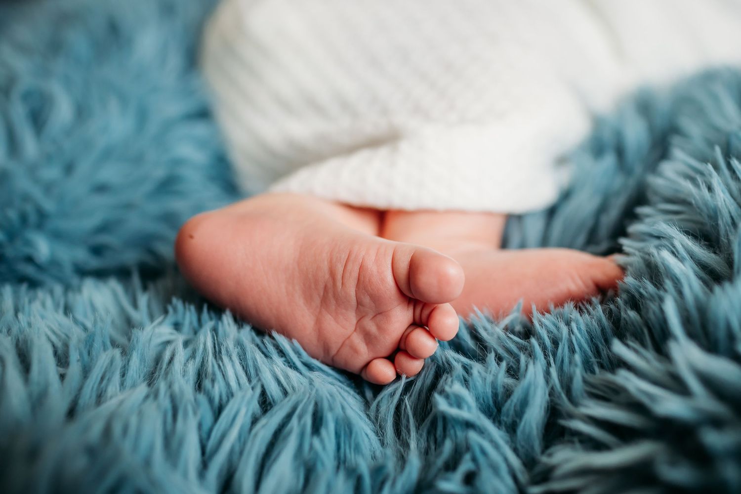 Close-up of tiny newborn baby feet resting on turquoise fluffy blanket.