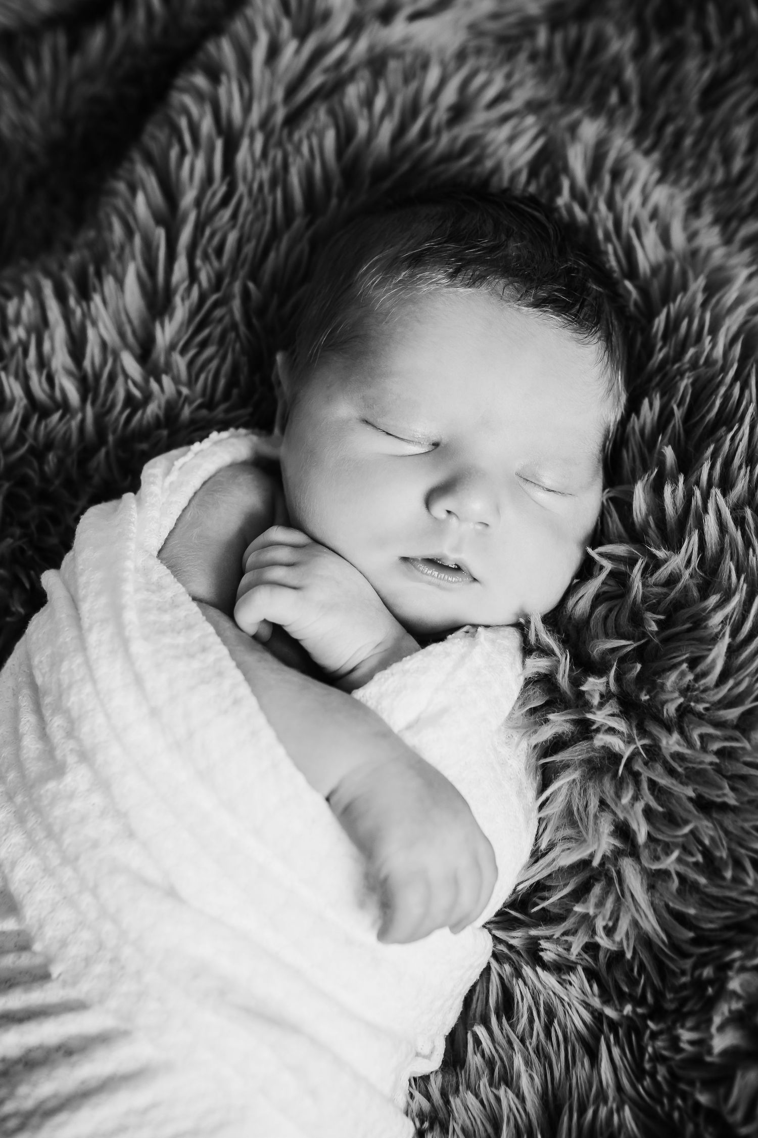 Peaceful newborn baby sleeping on fluffy gray blanket in black and white.