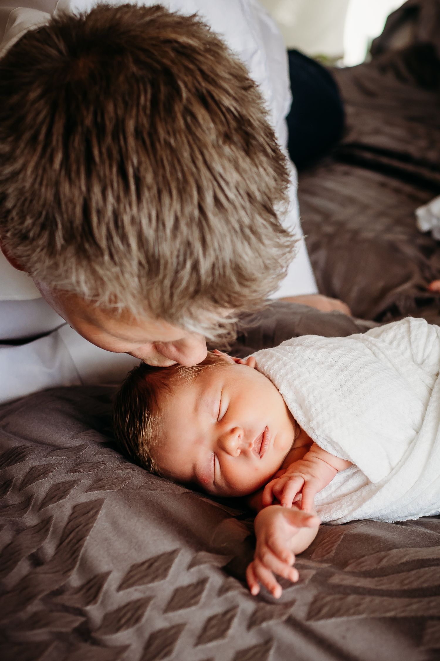 Tender moment of affection with sleeping newborn baby wrapped in white blanket.