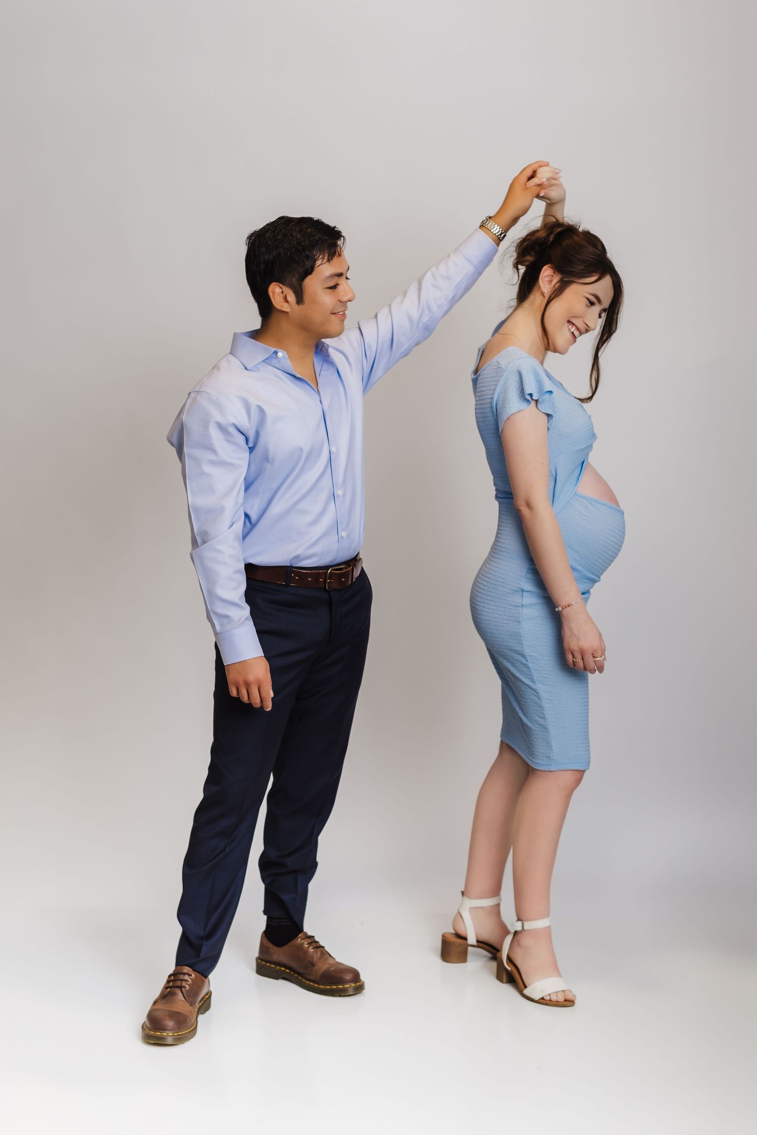 A couple posing playfully in formal attire against a neutral background.