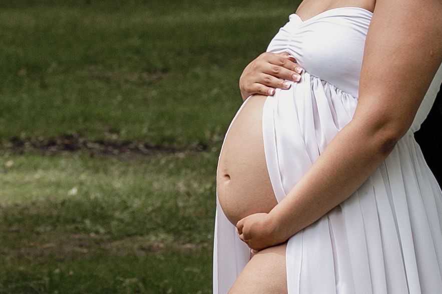 Close-up shot of a pregnant belly in a flowing white maternity dress.