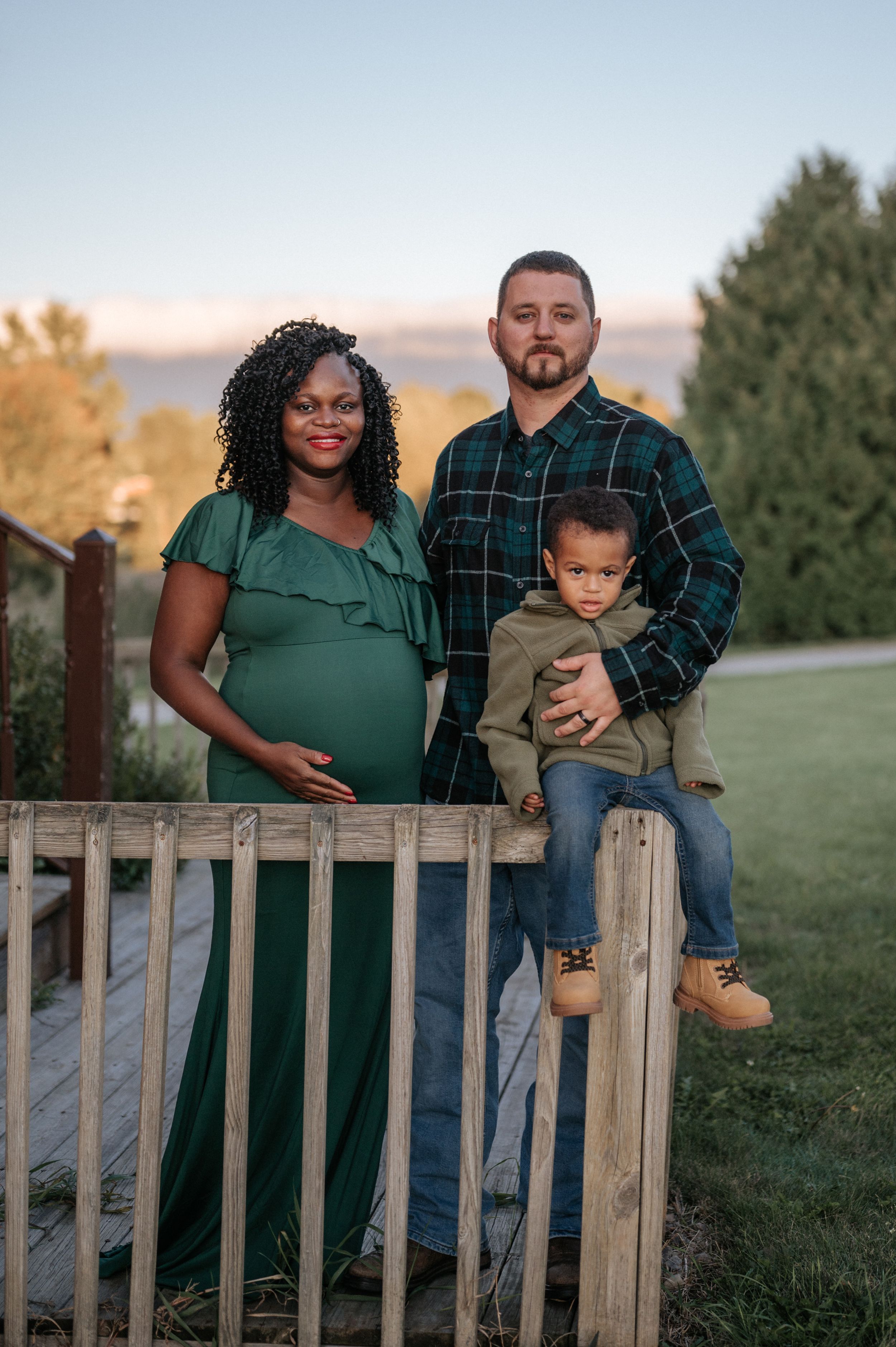 A family maternity portrait on a wooden deck with mountains and trees in the background.